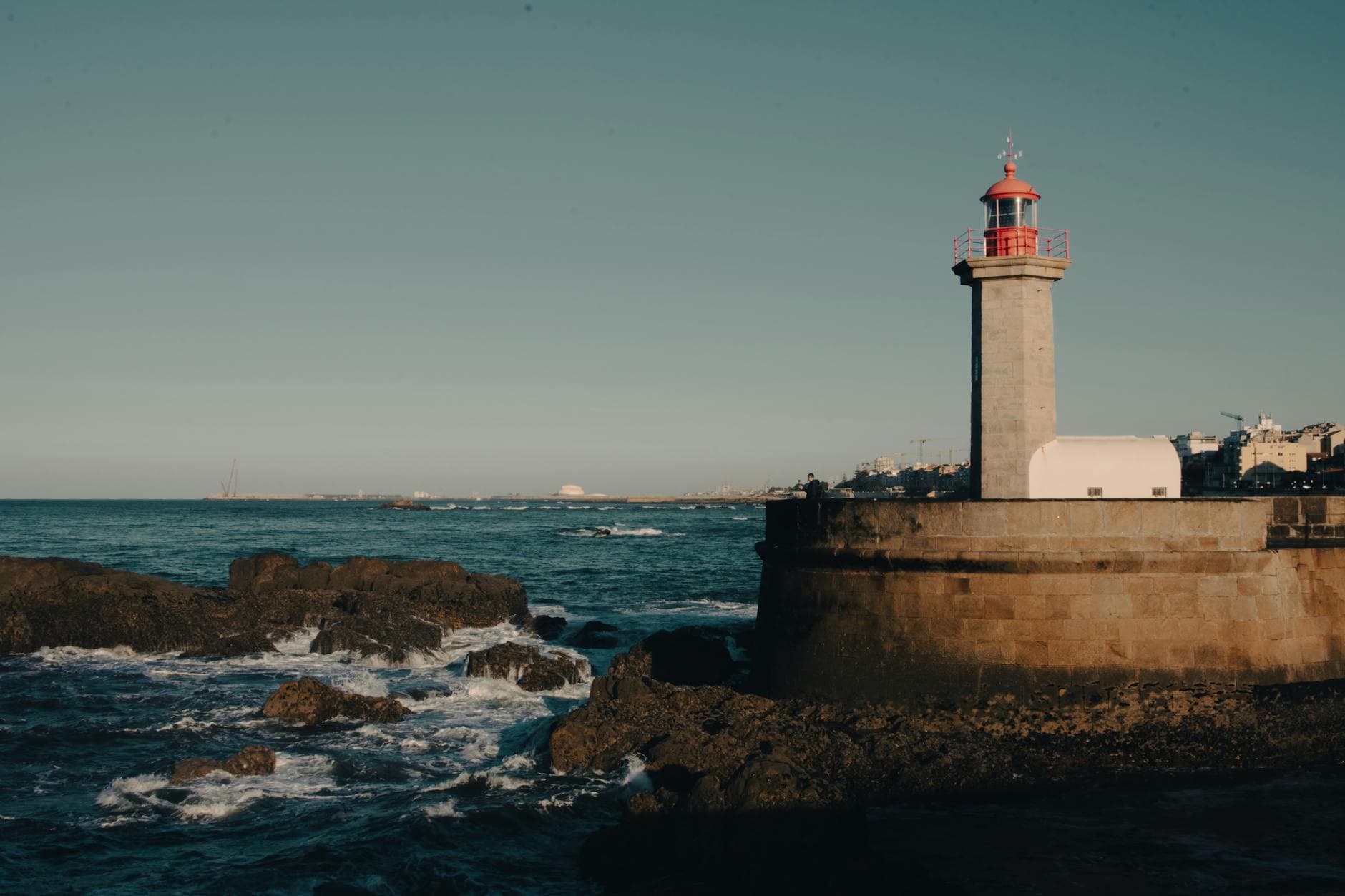 A scenic view of a historic lighthouse overlooking the Atlantic Ocean on Portugal's rocky coast in Porto.