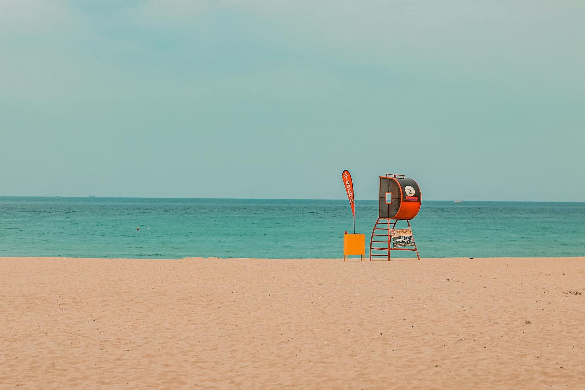 A tranquil view of a sandy beach in Donghae, South Korea featuring a lifeguard tower with a calm sea backdrop.