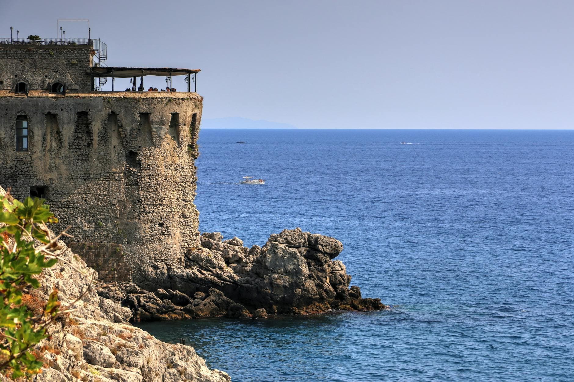 A historic stone tower overlooks the serene coastline of Sorrento, Italy, under a clear blue sky.