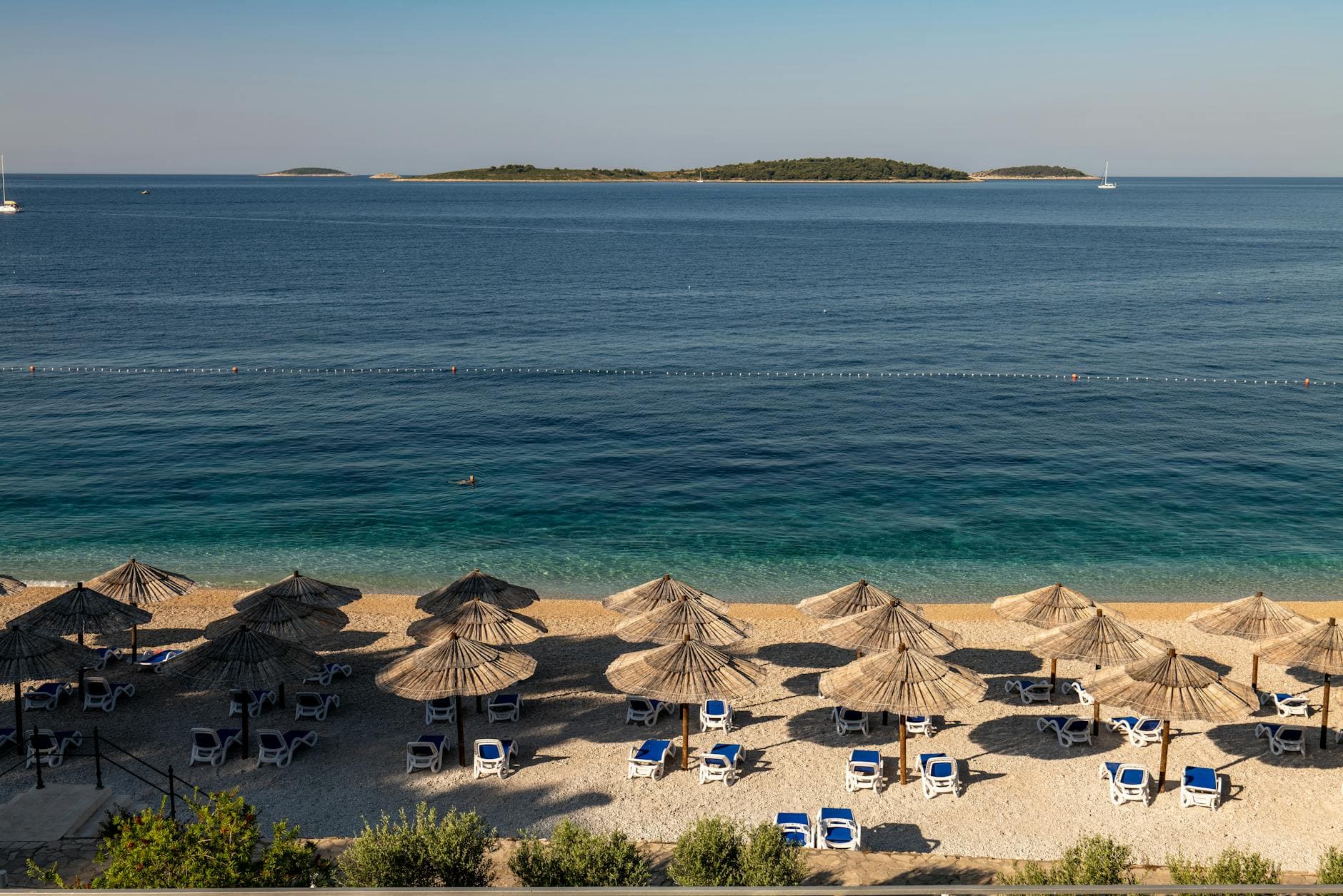 Aerial view of a sunny beach in Primošten, Croatia with umbrellas and loungers.