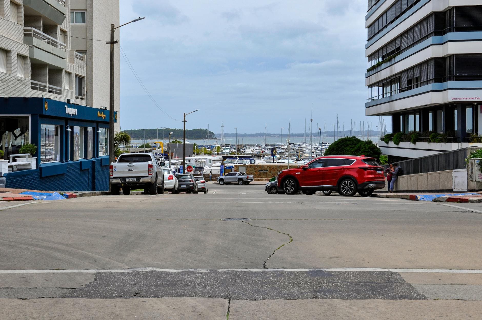View of Punta del Este's marina from a bustling urban street, featuring buildings and parked cars.