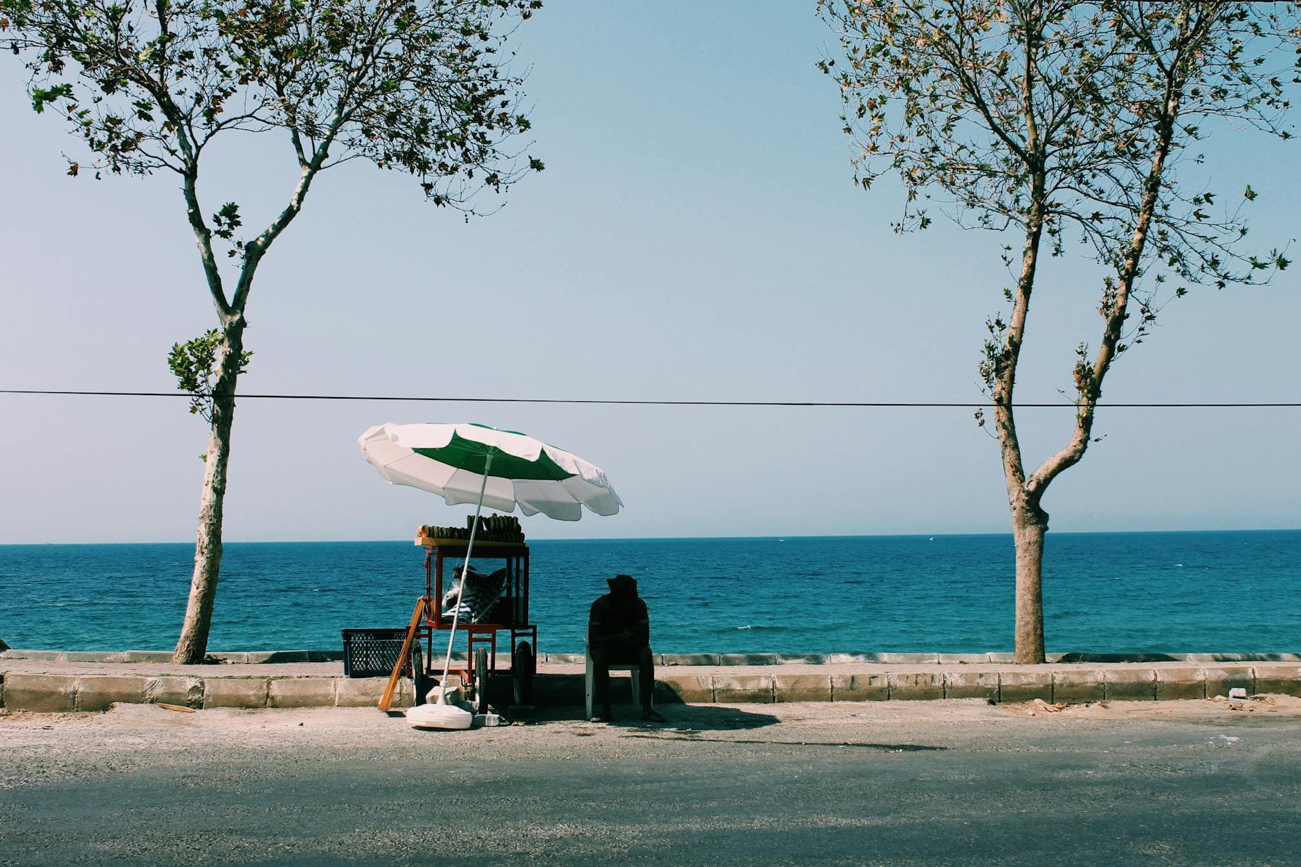 Peaceful oceanside scene with a street vendor under an umbrella by the beach. Tranquil and scenic.
