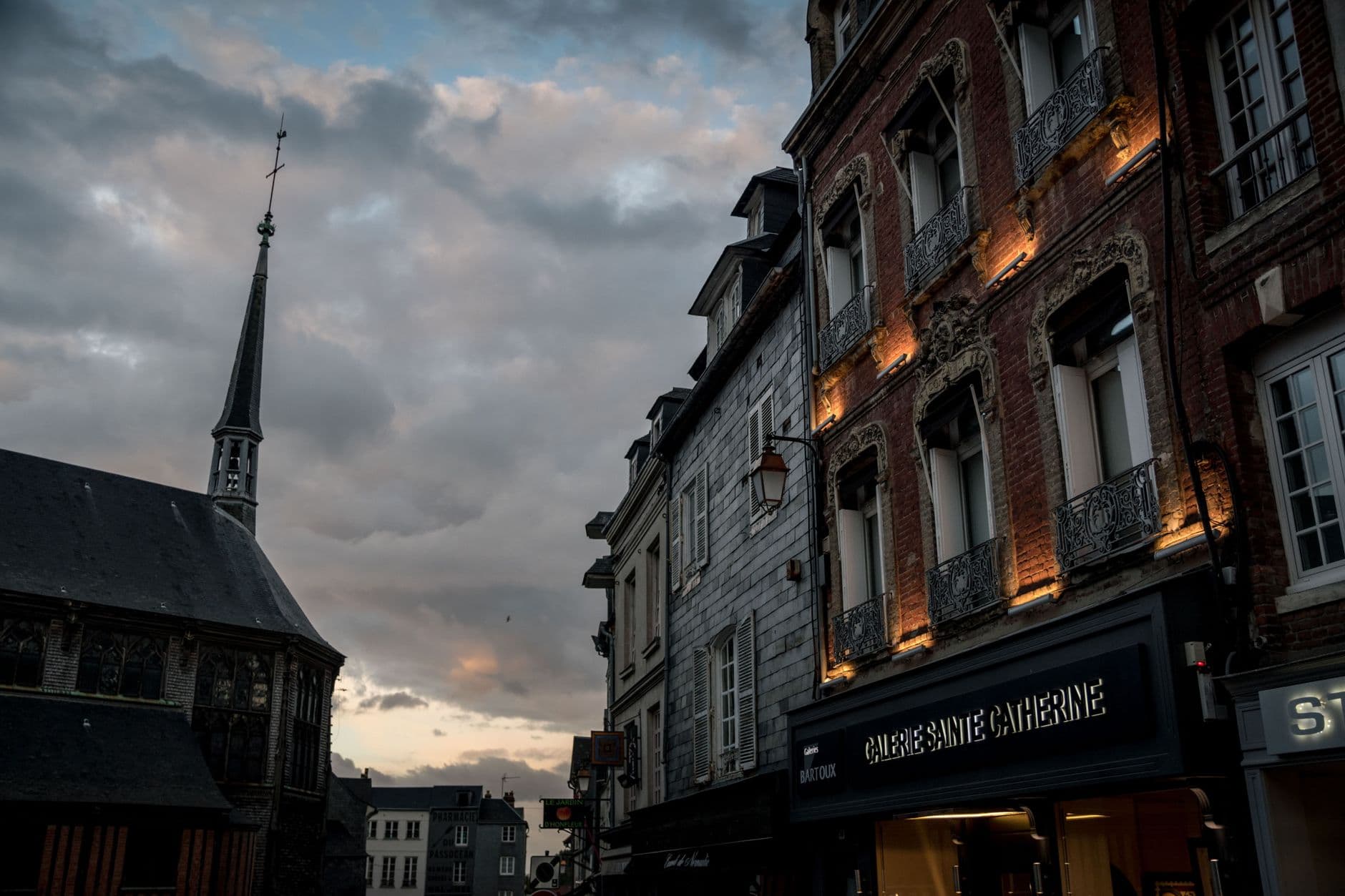 Evening view of historic buildings on a street in Honfleur, France featuring a cloudy sky and charming architecture.