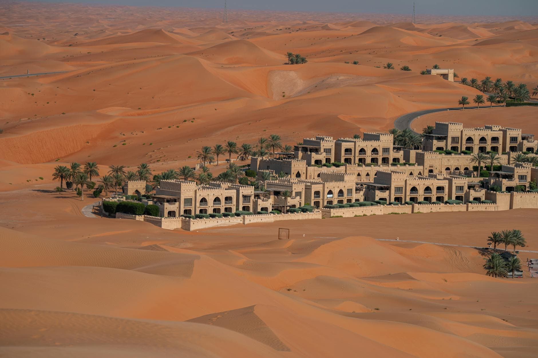 Explore the vast desert landscape of Abu Dhabi with this aerial view showcasing a luxurious hotel surrounded by sand dunes.
