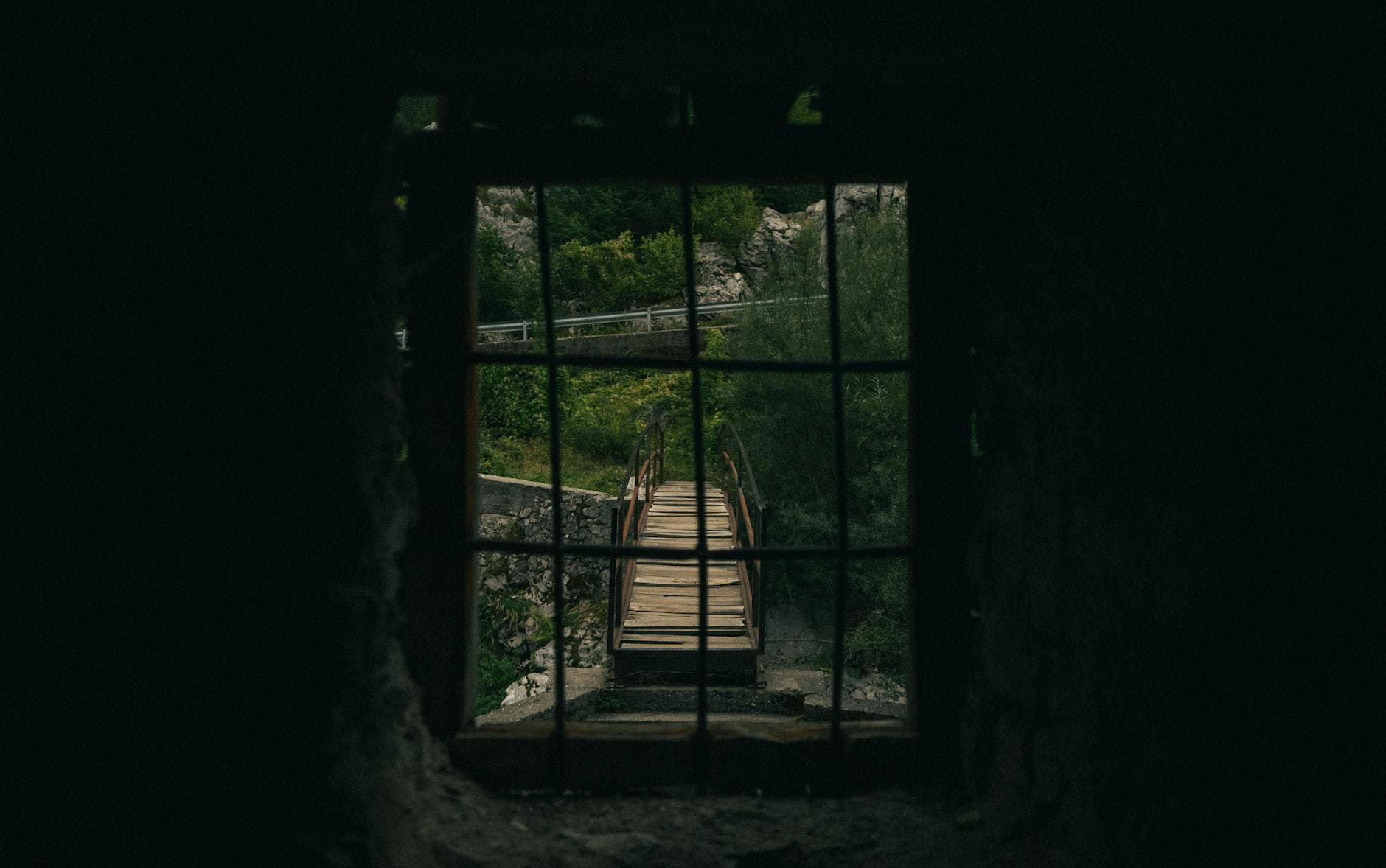 View of a rustic wooden bridge through an ancient window in Valbonë, Albania.