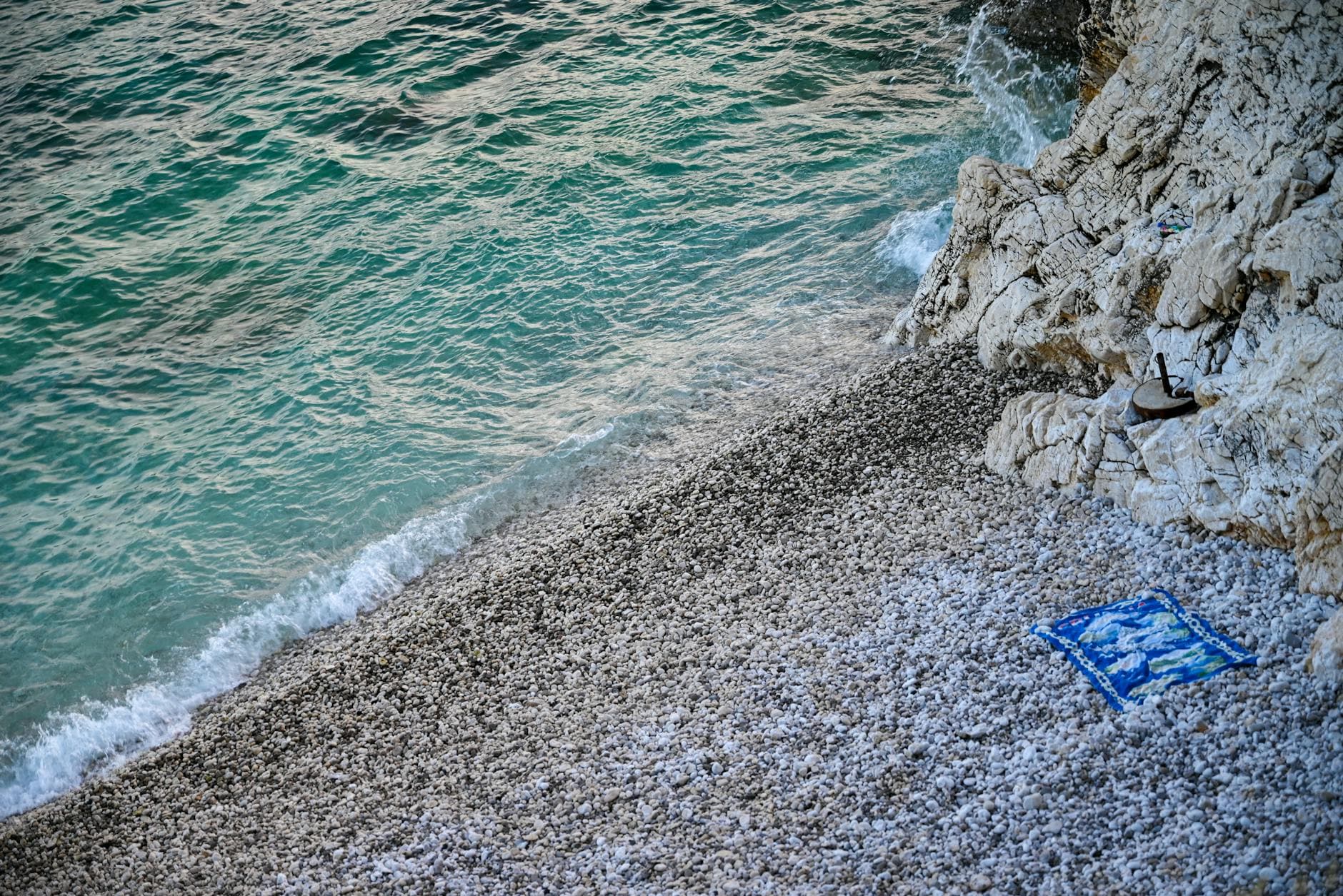 A scenic view of the pebbled beach and turquoise sea in Rabac, Croatia with rocky shoreline.
