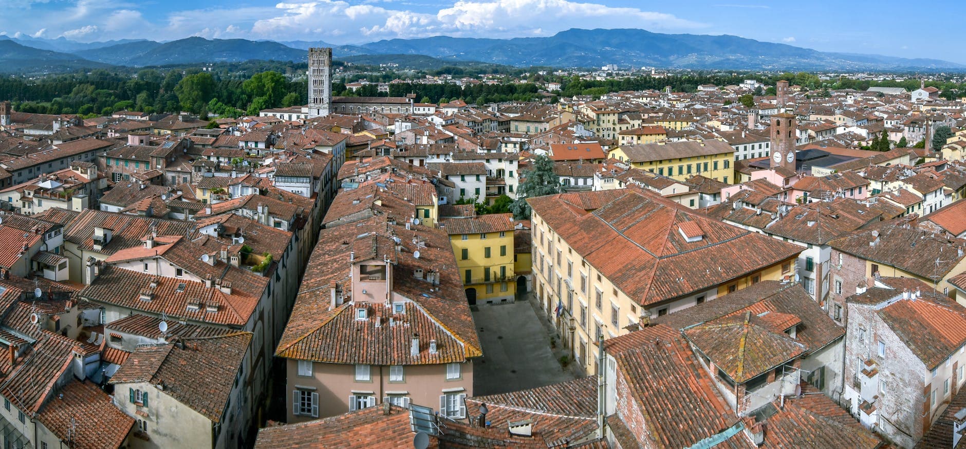 Aerial view of Lucca's historic rooftops and towers under a bright blue sky.