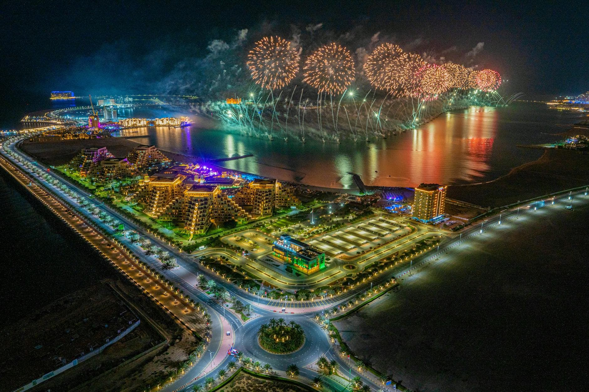 A breathtaking aerial view of fireworks over Ras al Khaimah's illuminated coastline at night.