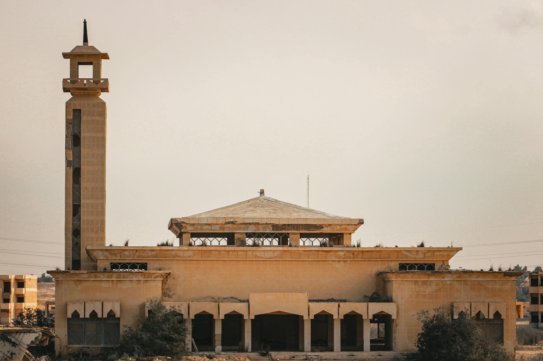 A scenic view of a historic mosque with a tall tower against a barren landscape under a hazy sky.