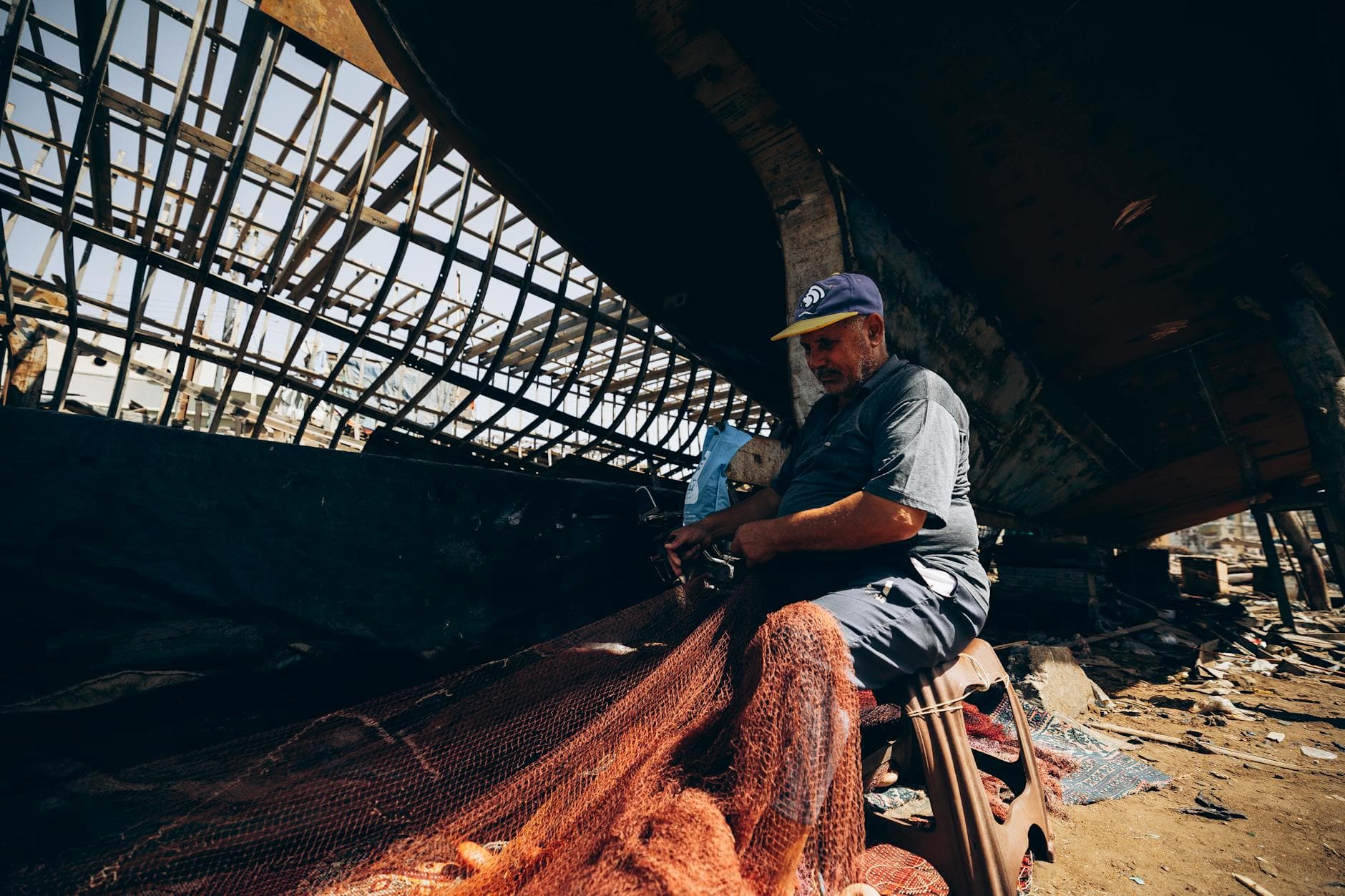 A fisherman in Damietta, Egypt, skillfully repairing nets under a boat, showcasing daily life by the shore.
