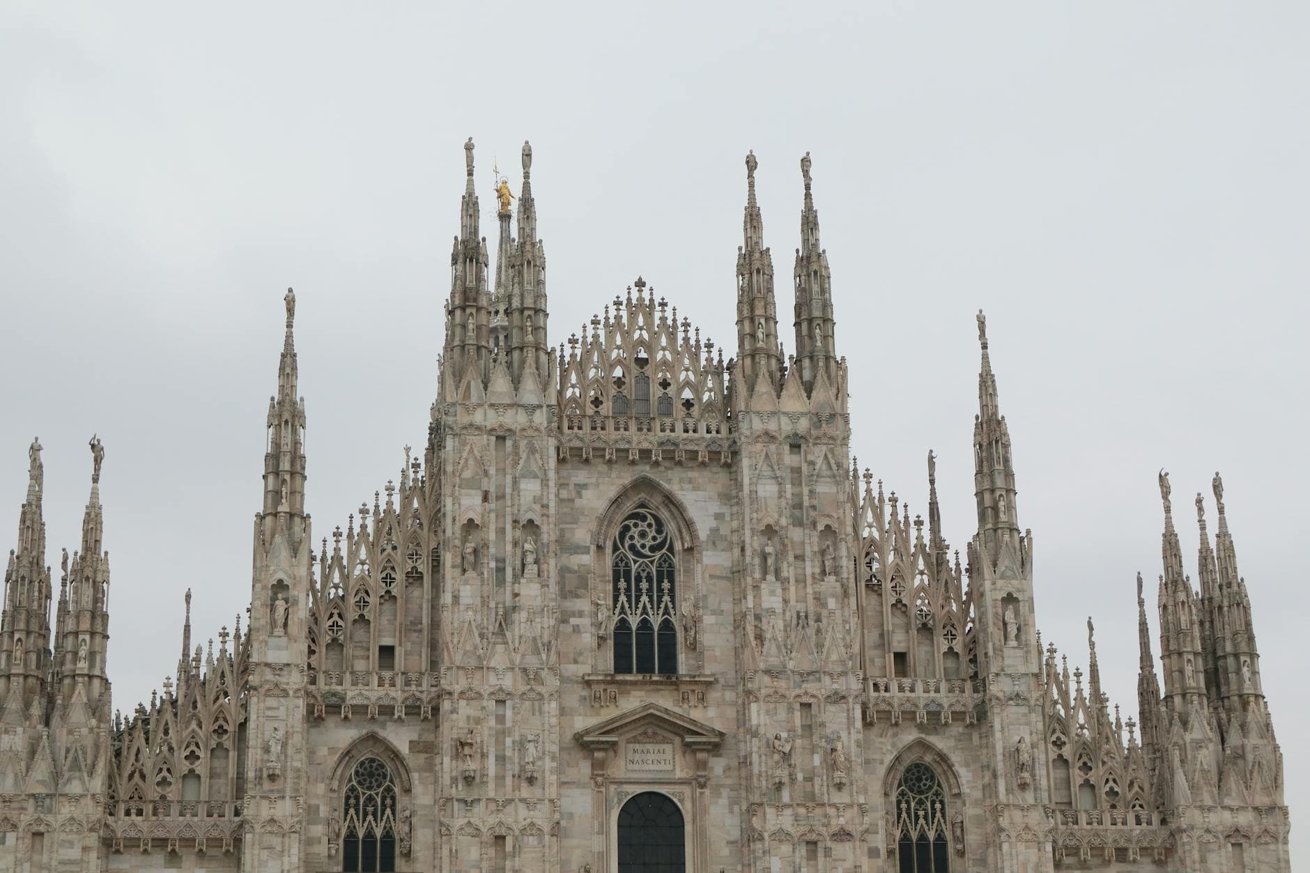 Capture of the striking facade of Milan Cathedral showcasing Gothic architecture under a cloudy sky.