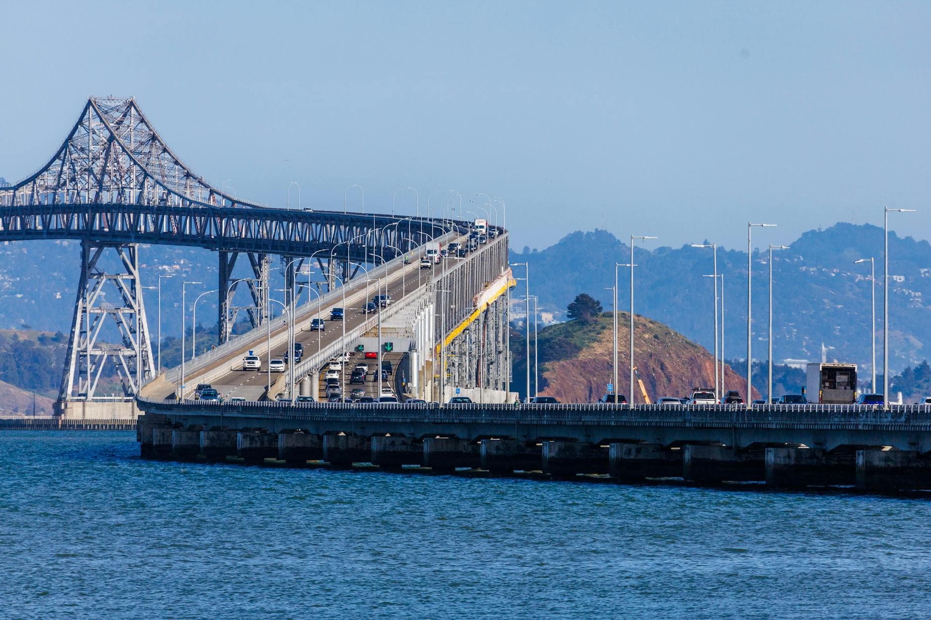 View of the Richmond-San Rafael Bridge with vehicles crossing over a body of water, surrounded by hills.