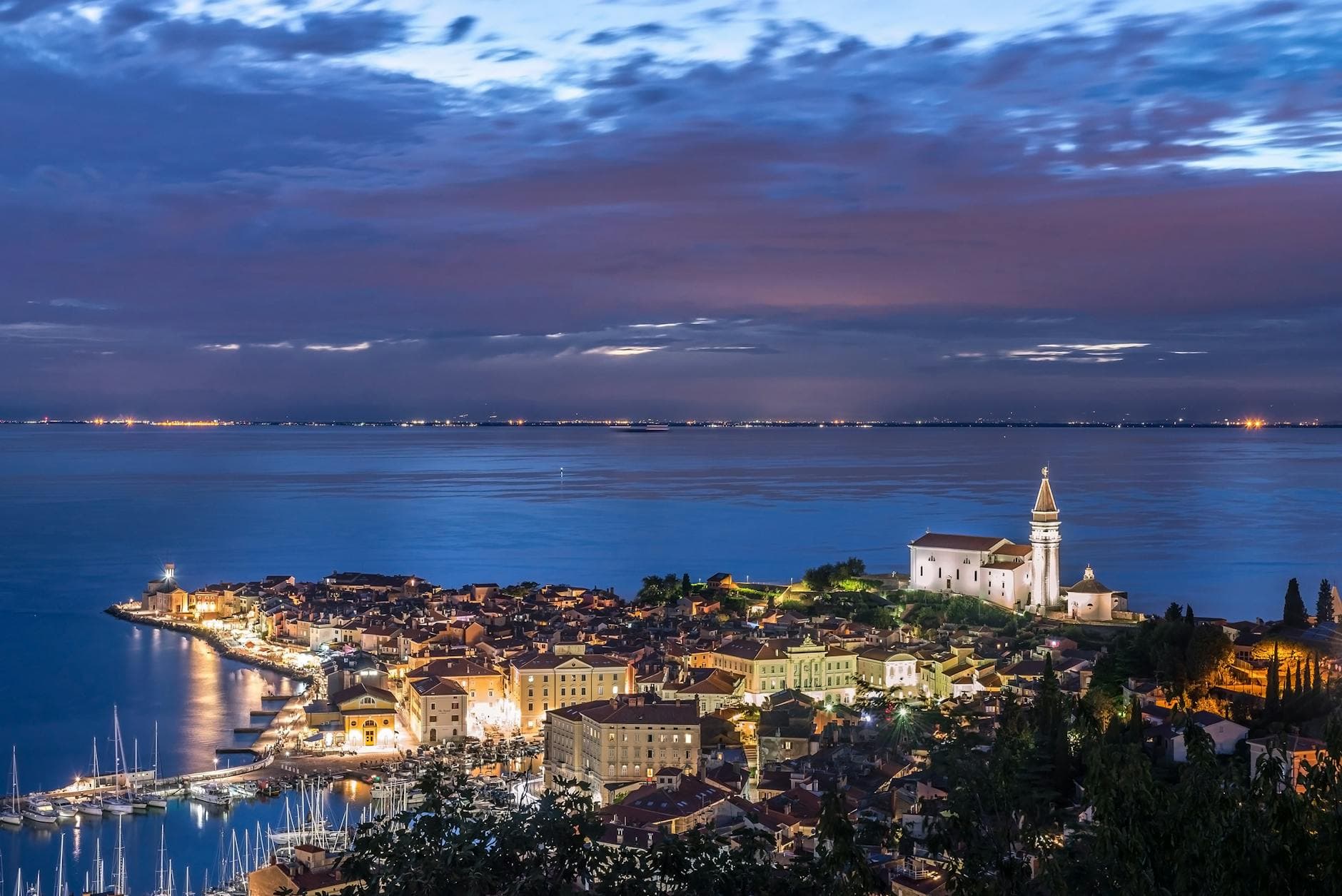 A stunning aerial view of a coastal town with illuminated harbor and church at twilight, capturing serene beauty.