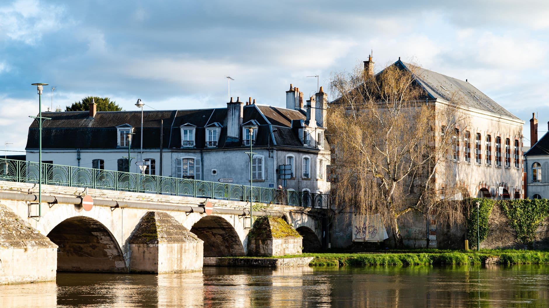 Scenic view of a historic bridge and buildings in a French town under a cloudy sky.