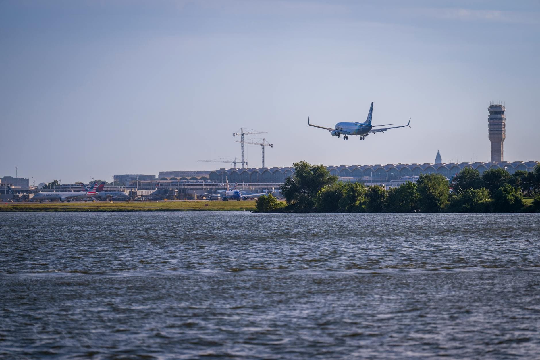 Airplane approaches Ronald Reagan Washington Airport over the Potomac River, with control tower and terminal in view.