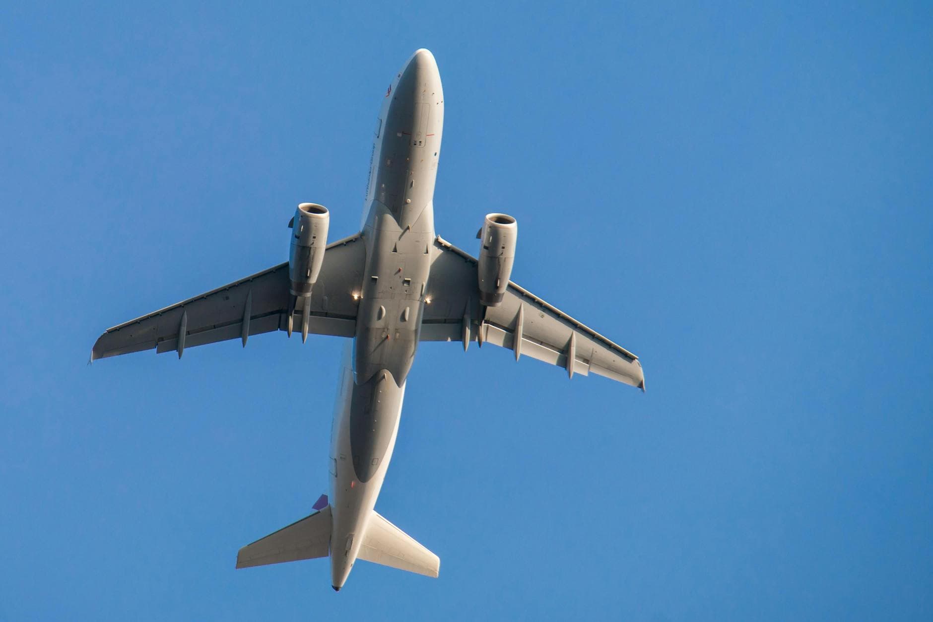 A commercial airplane taking flight, viewed from below against a clear blue sky.