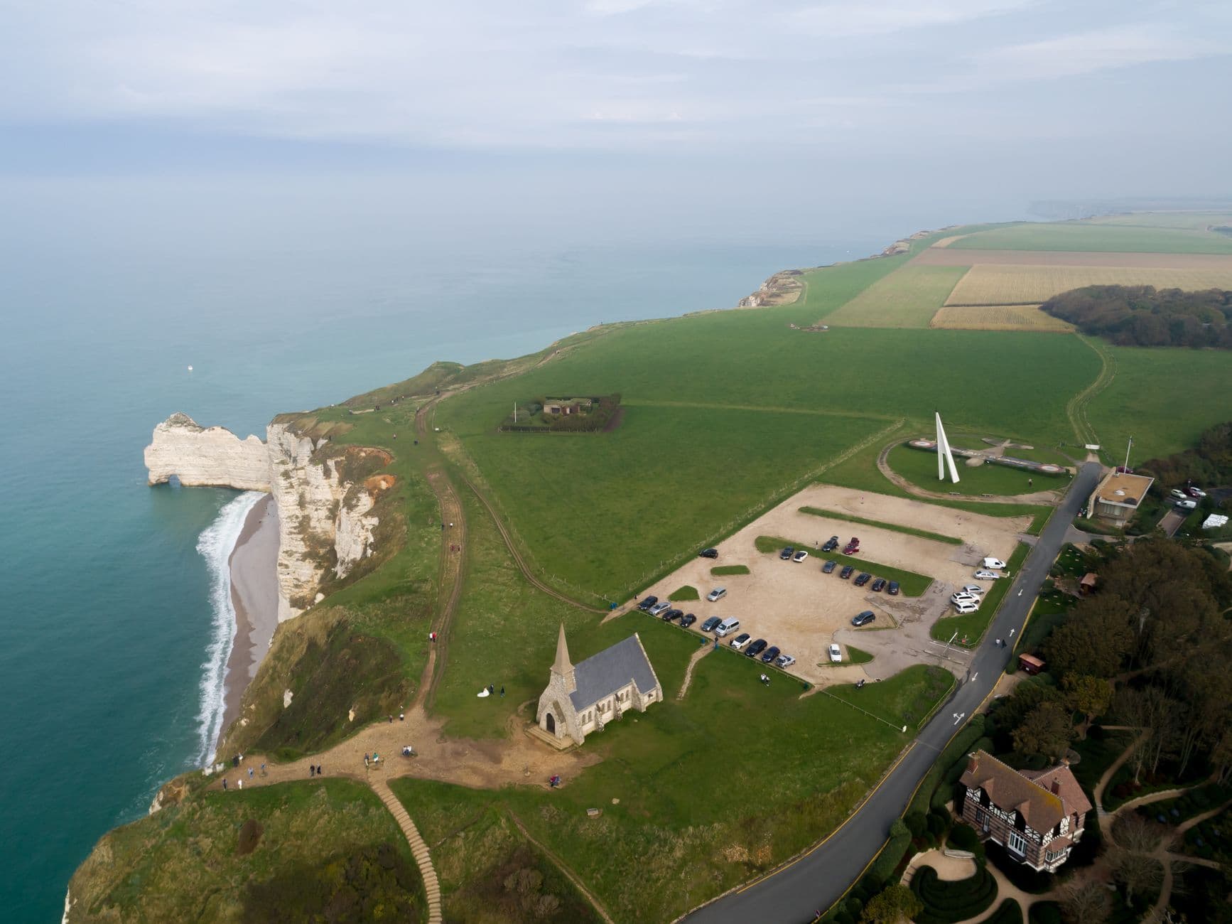 Scenic aerial view of a coastal cliff with a historic church, lush fields, and sea in the background.