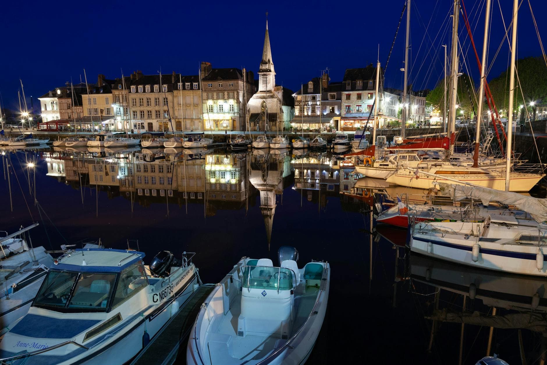 A serene view of Honfleur's marina with boats and historic buildings reflecting in the water at night.