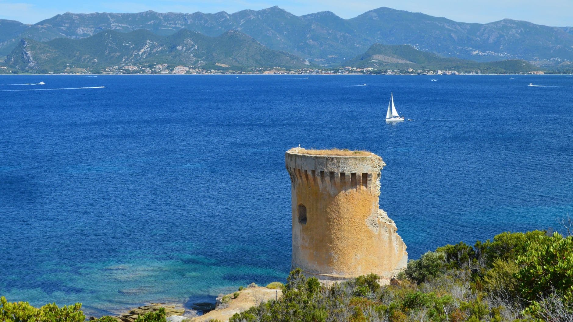 Beautiful view of Saint-Florent, Corse, featuring a historic tower by the seaside and distant mountains.