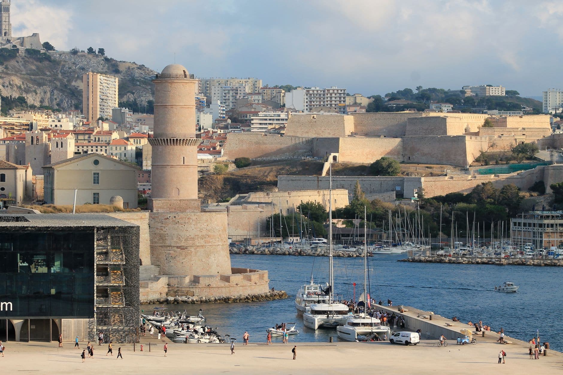Scenic view of Marseille's historic Fort Saint-Jean and vibrant harbor in France, capturing urban architecture and waterfront activity.