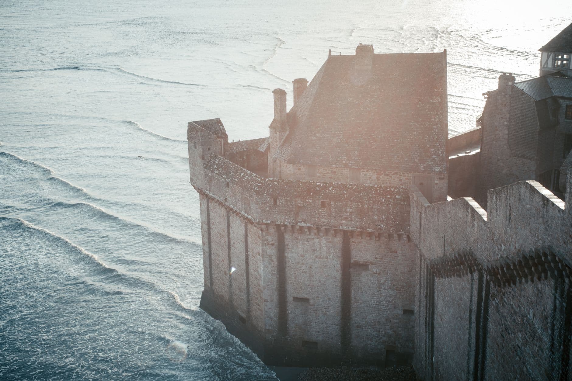 A stunning aerial view of a medieval fortress on the coast at sunrise, capturing the serene sea and historic architecture.
