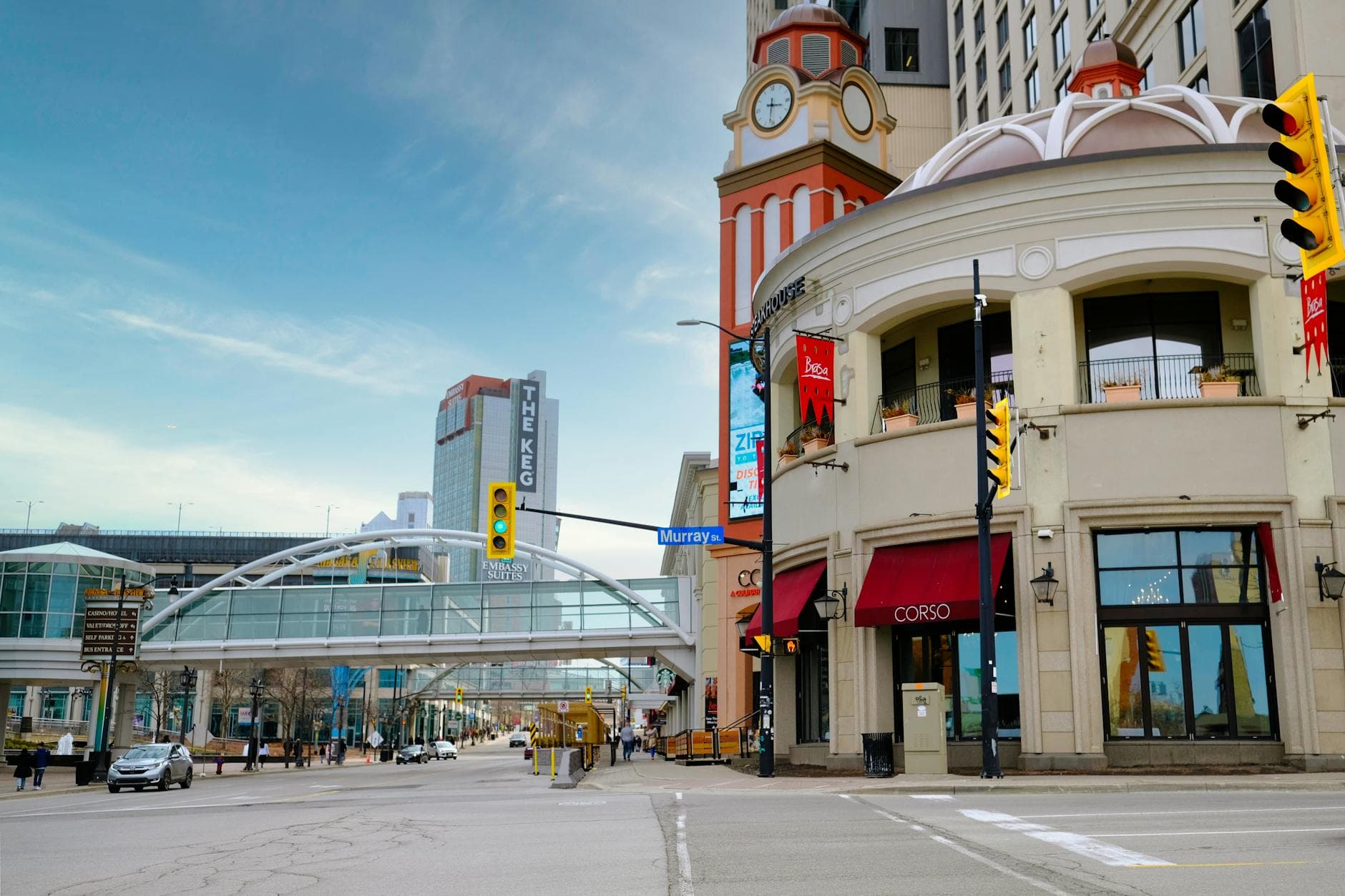Cityscape featuring a footbridge, modern skyscrapers, and a classic clock tower in a lively urban setting.