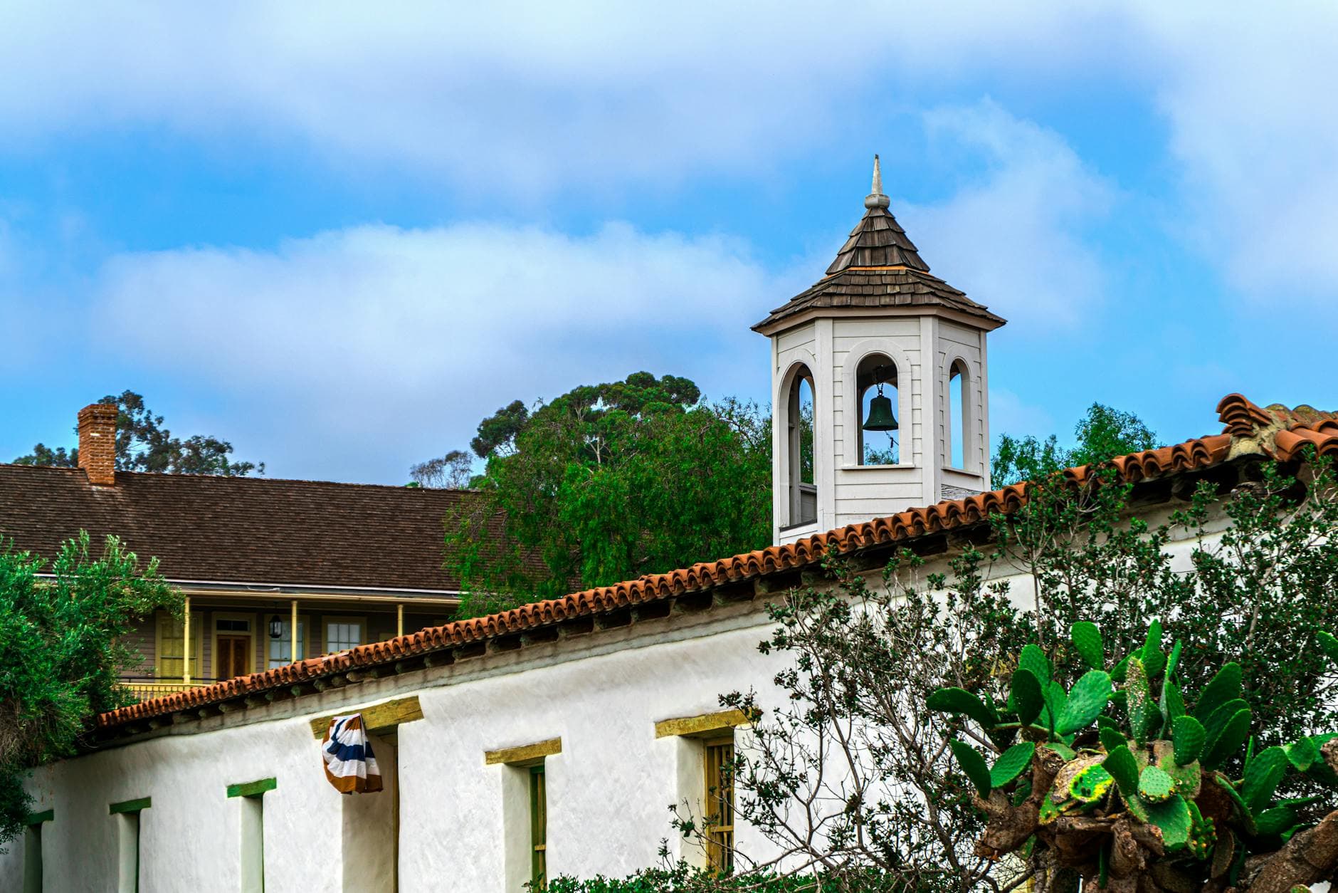 A picturesque view of a historic mission bell tower surrounded by lush greenery in San Diego, CA.