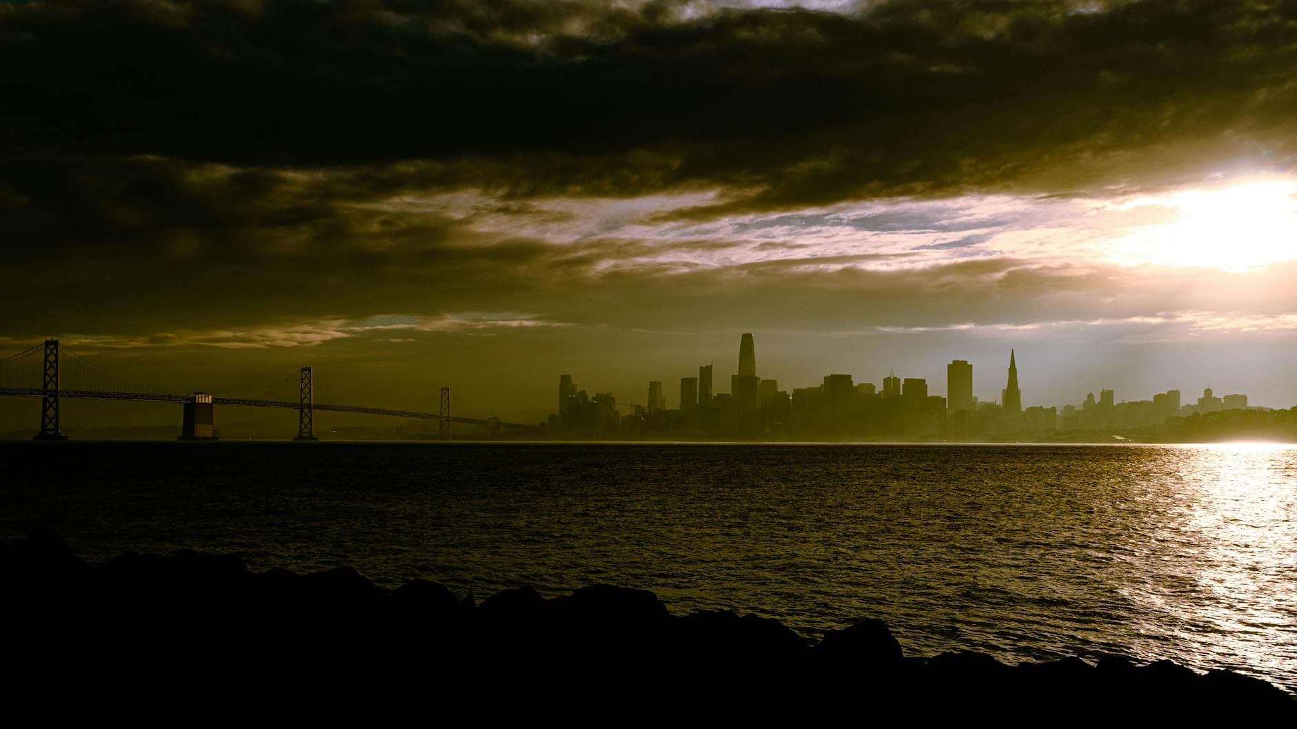 Dramatic sunset over San Francisco Bay with skyline and Bay Bridge silhouette.