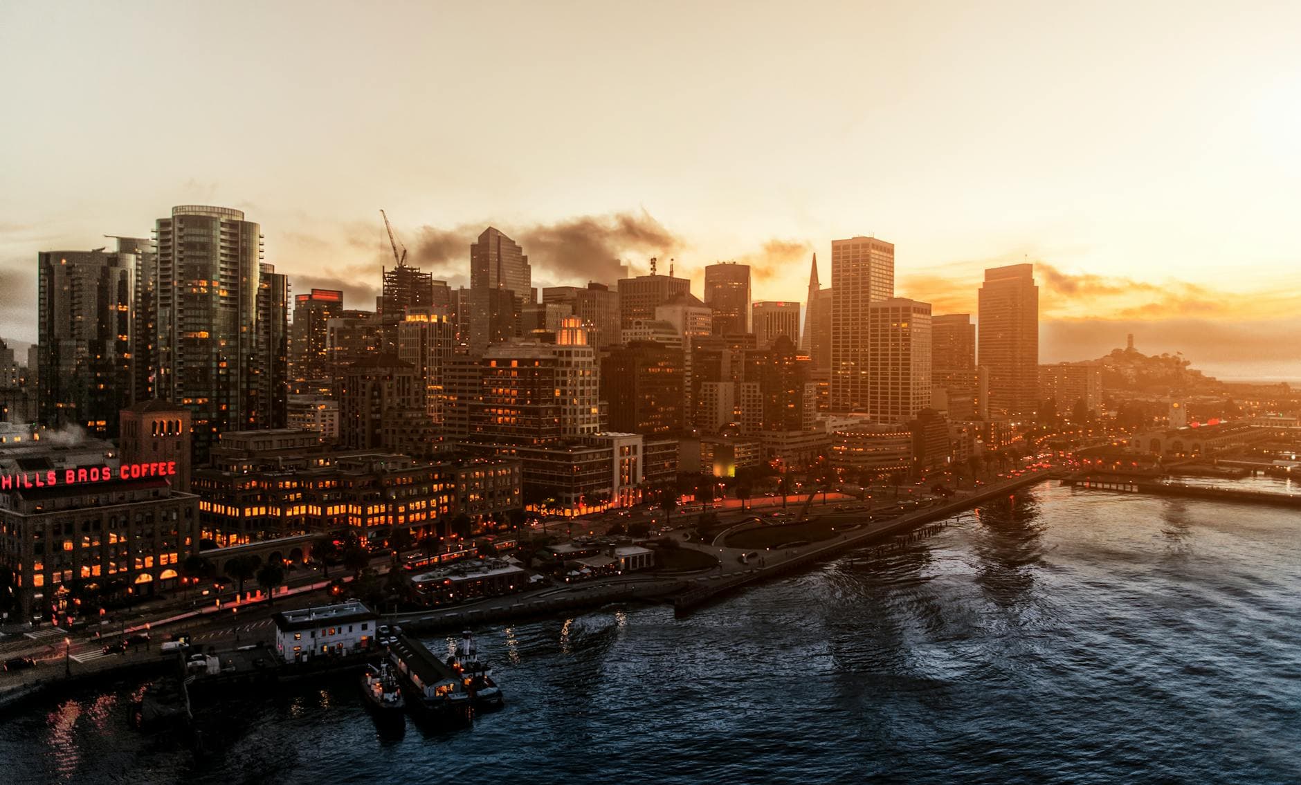 Dramatic aerial view of San Francisco's illuminated skyline during sunset, reflecting on the bay waters.