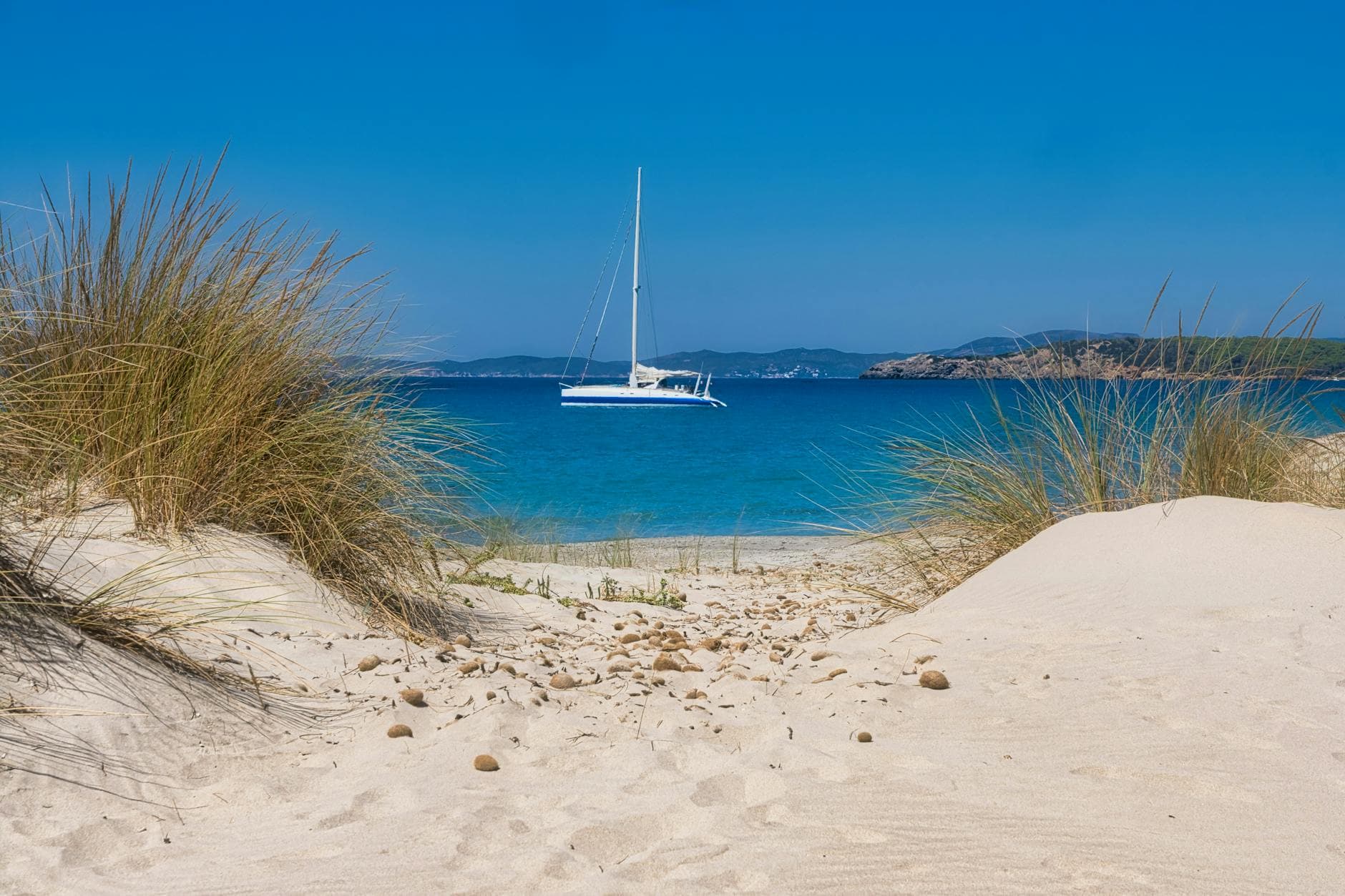 Idyllic beach view with a sailboat on clear blue water at Porto Pino, perfect summer escape.