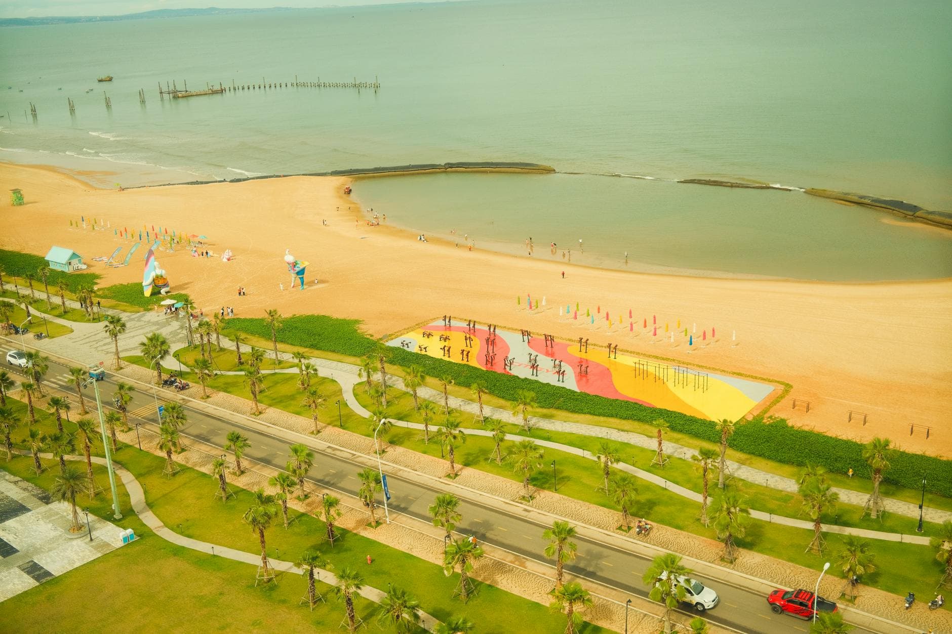 Aerial view of a vibrant seaside resort with colorful parasols and palm-lined streets.