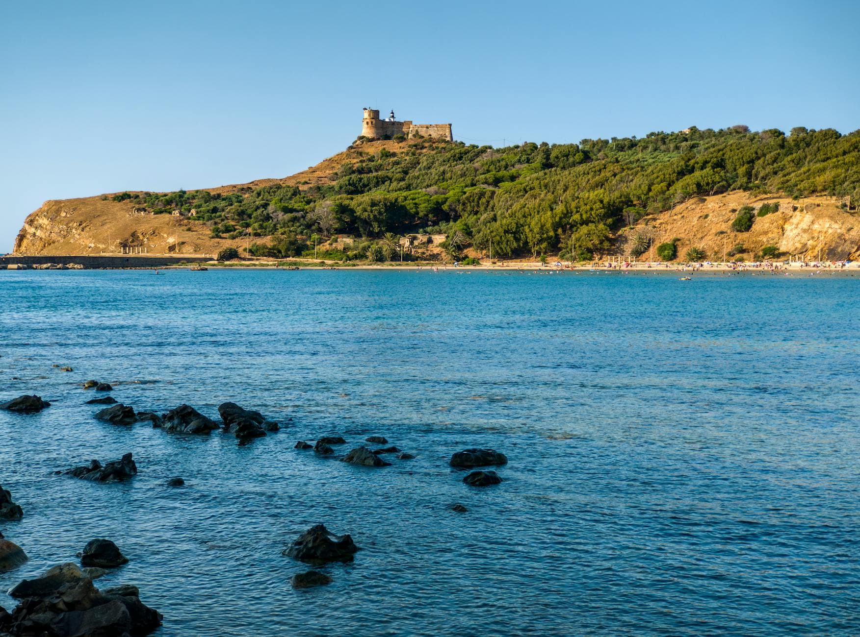 Beautiful coastal landscape featuring a historic castle atop a lush hillside beneath a clear blue sky.