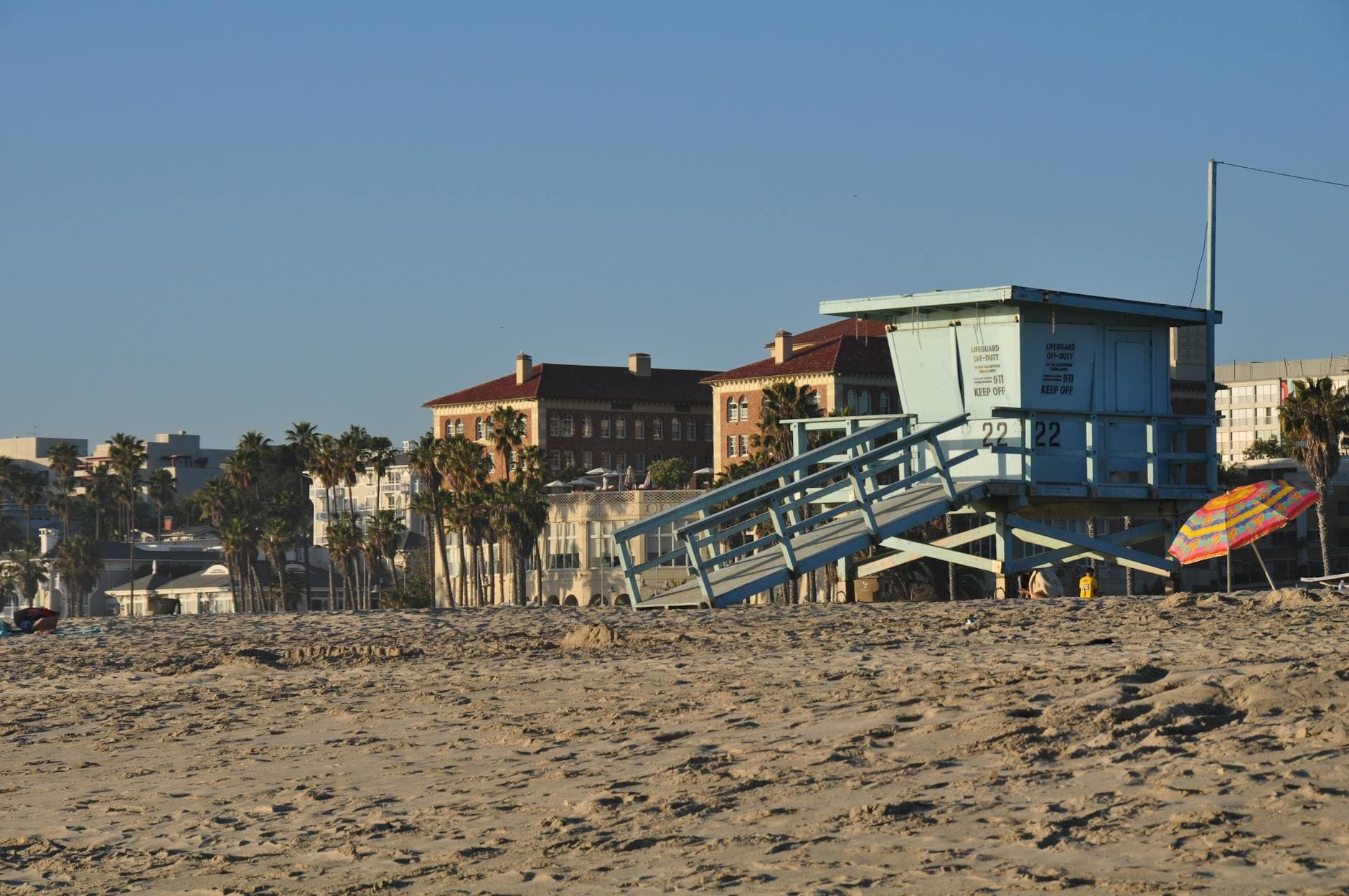 Lifeguard tower on Santa Monica beach with colorful umbrella and buildings in the background.