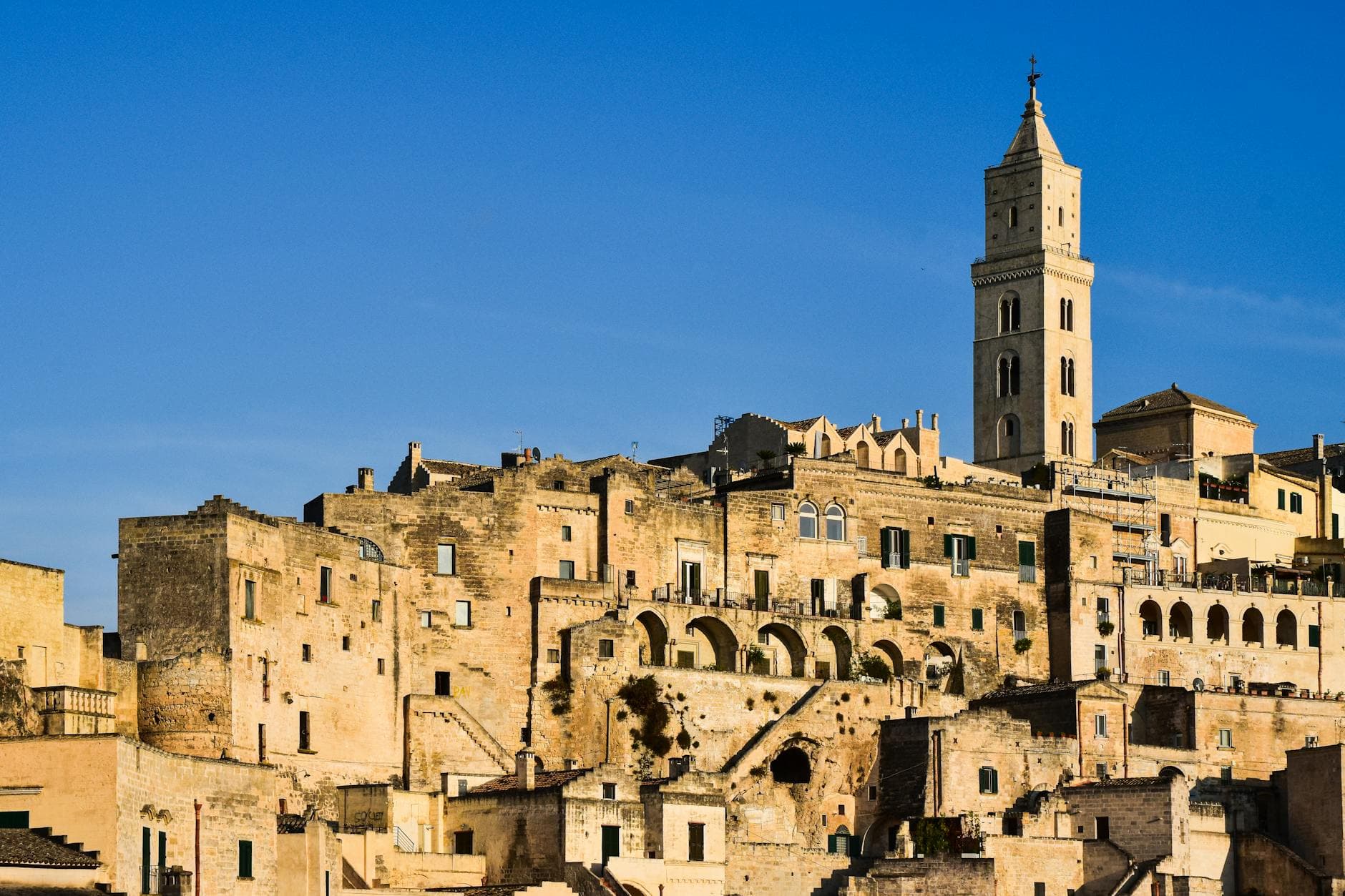 Captivating view of Matera's ancient buildings and bell tower in warm sunset light.