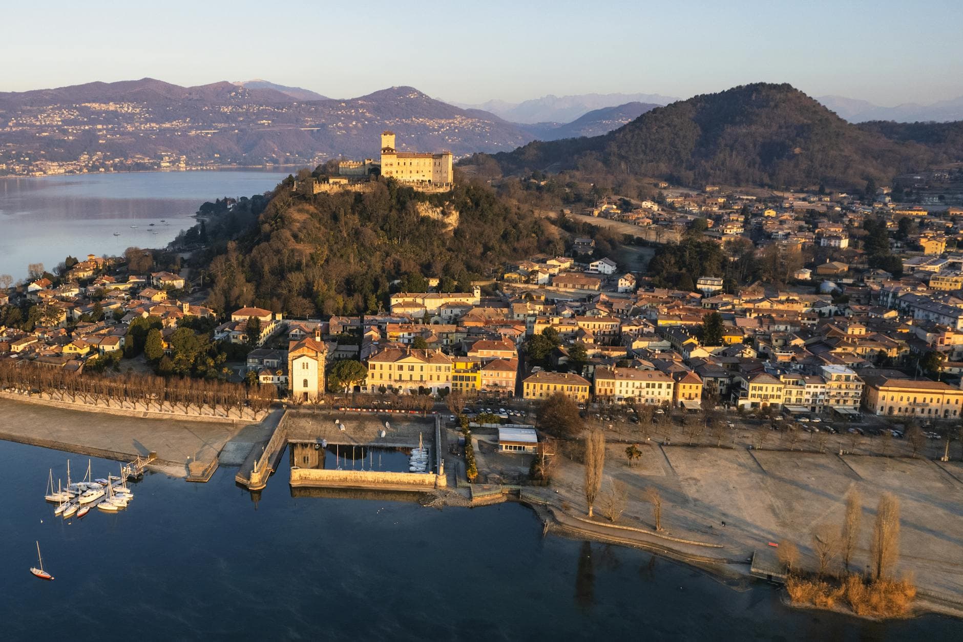 A breathtaking aerial view of Angera, Italy, showcasing the historic Rocca di Angera and serene Lake Maggiore at sunset.