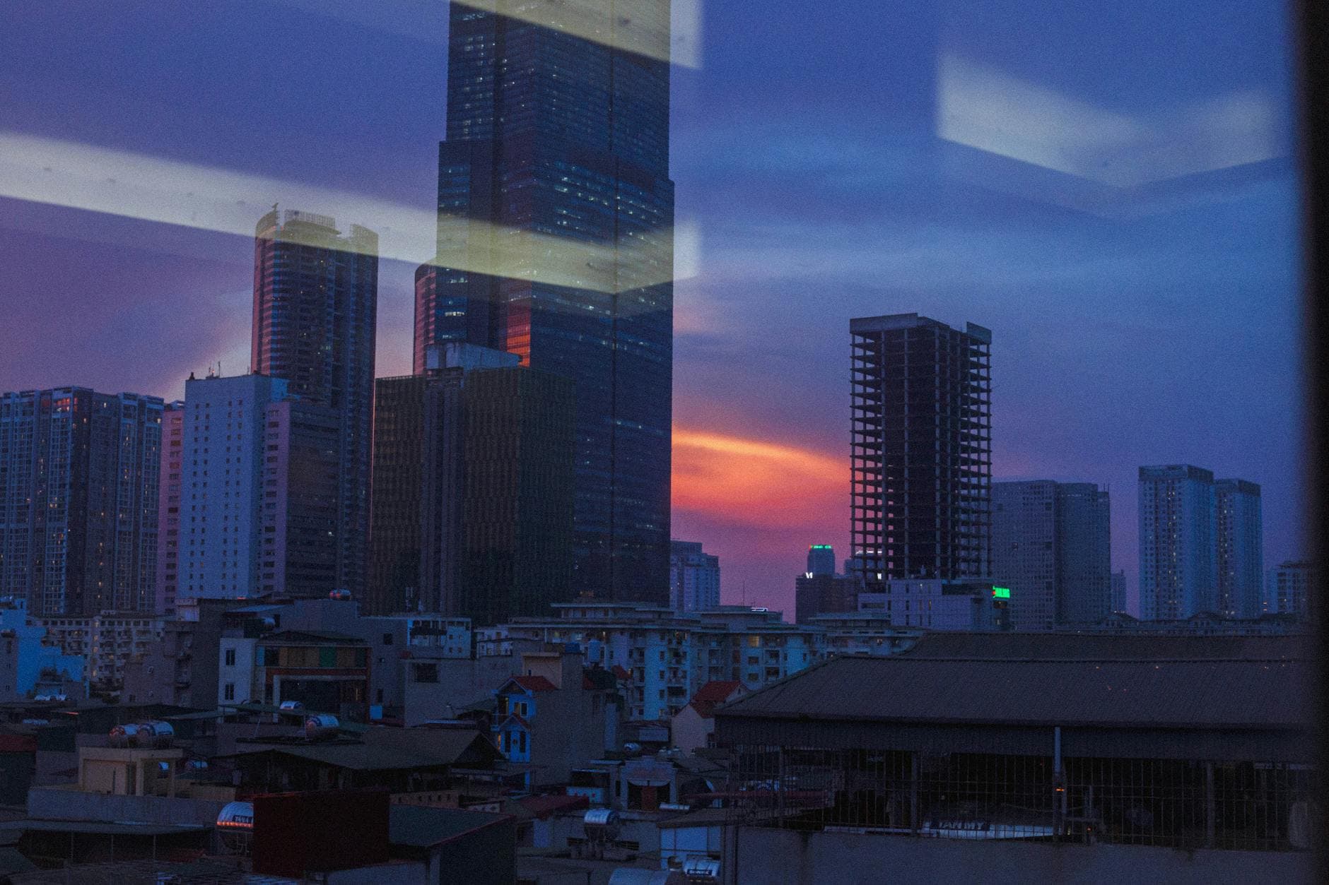 Dramatic view of a city's towering skyscrapers during twilight, reflecting vibrant sunset hues.