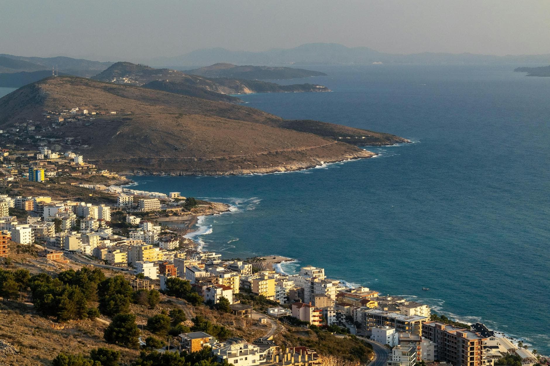 A stunning aerial view of Sarandë, Albania, featuring dramatic coastline and cityscape at sunset.