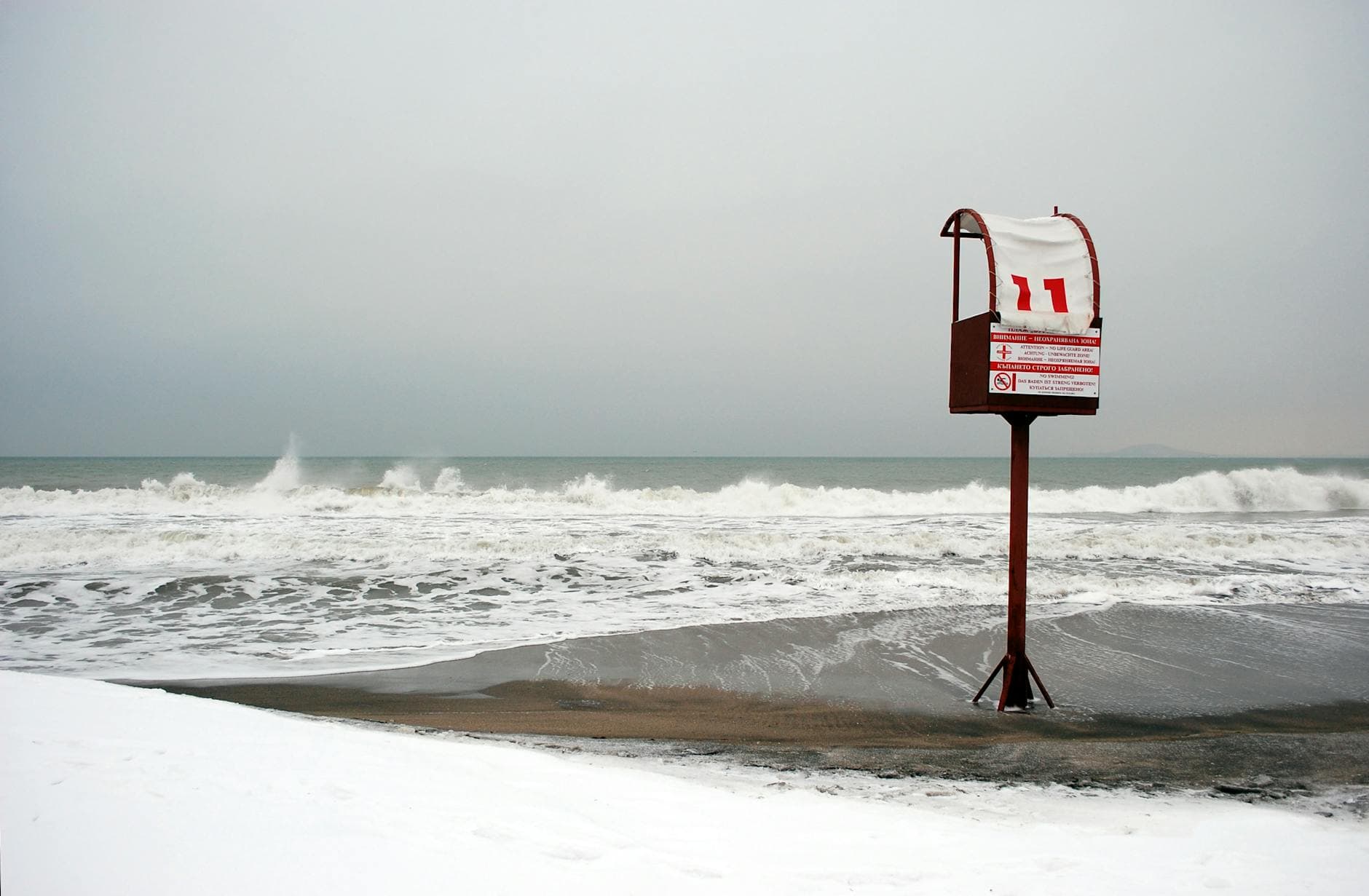 A snowy beach scene with waves crashing and a lifeguard station, capturing winter at the coast in Burgas, Bulgaria.