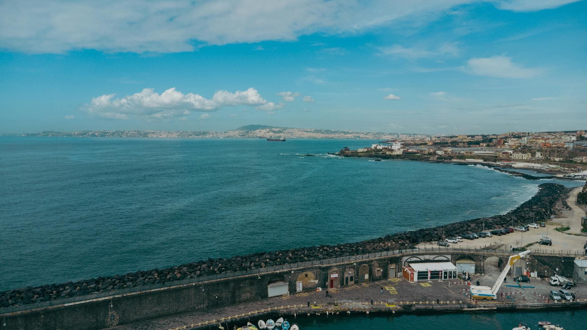 Stunning aerial view of the Napoli coastline featuring the bay, cityscape, and distant mountains under a blue sky.