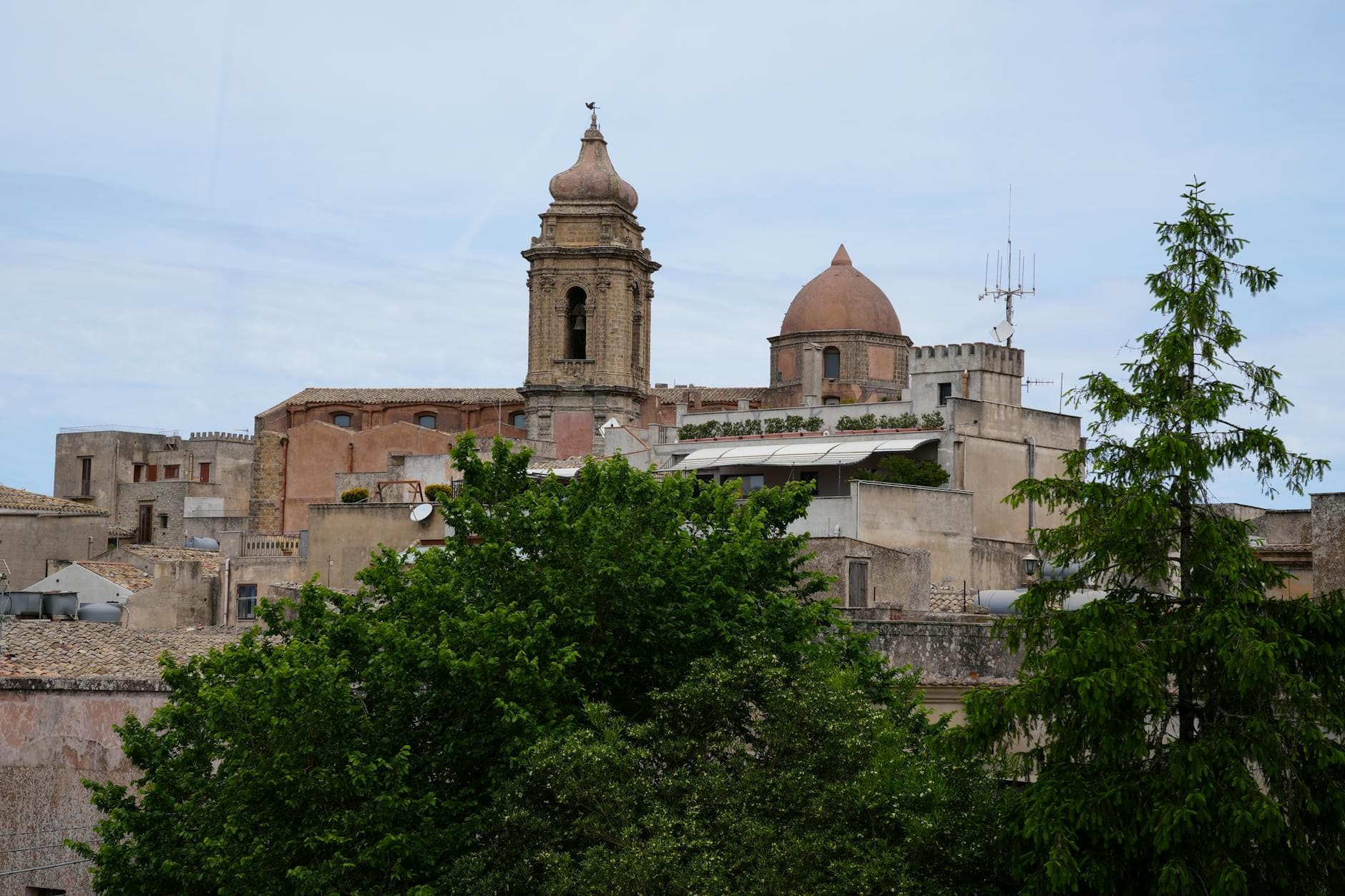 View of historic church and architecture in Erice, Sicily with greenery in foreground.