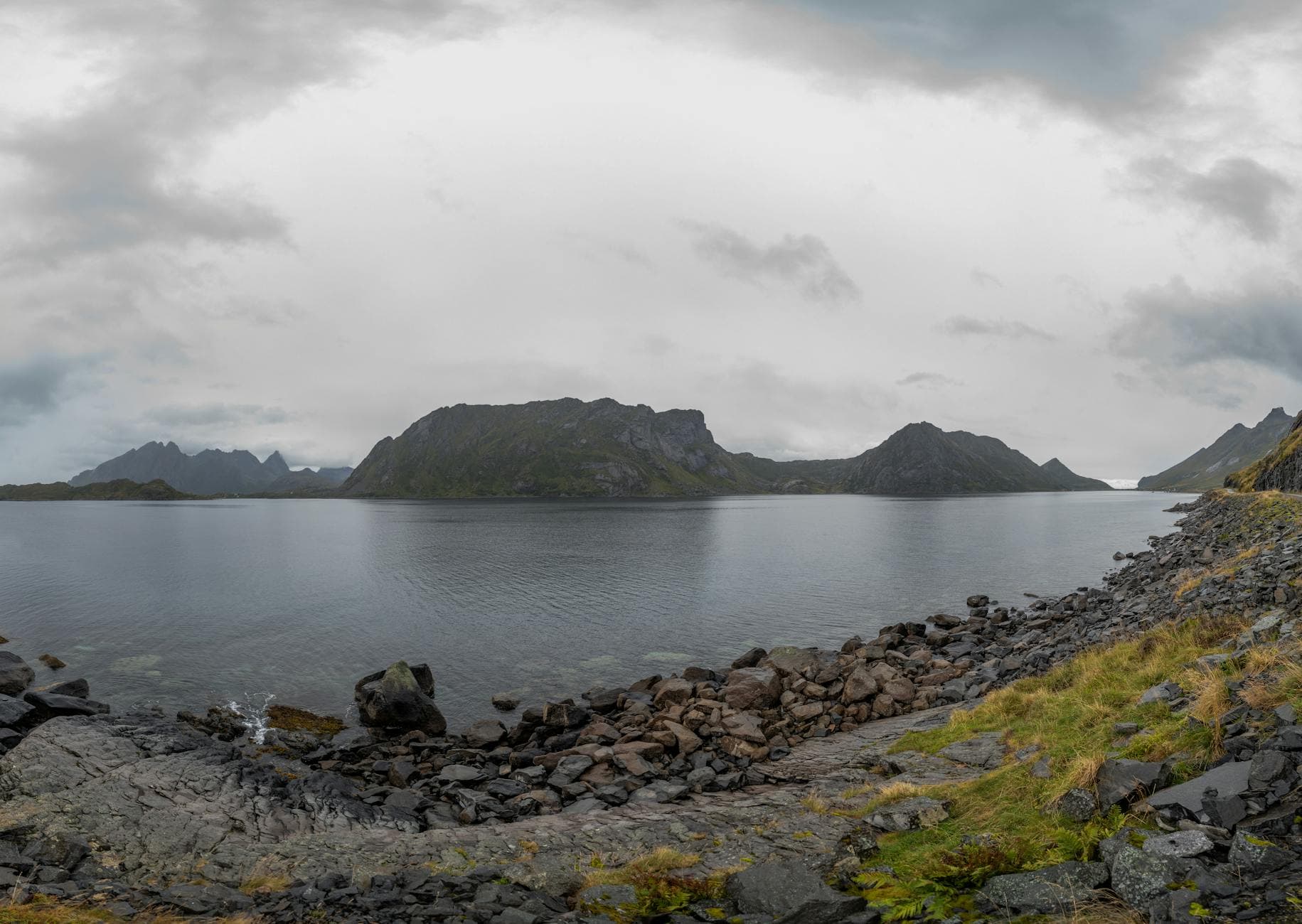 Picturesque view of rough stony shore surrounded by calm water under gray cloudy sky