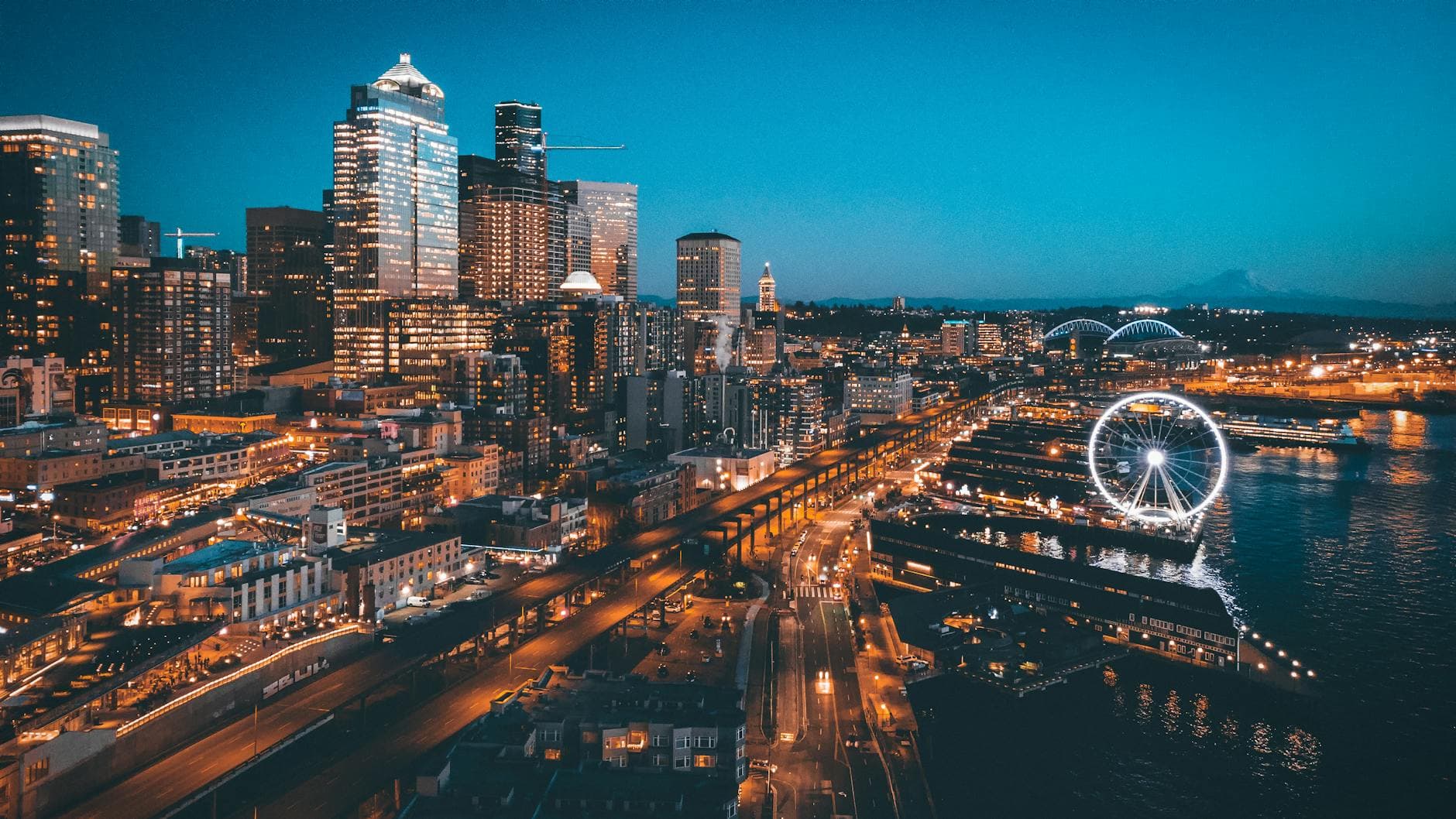 A stunning aerial view of Seattle's skyline at night featuring the illuminated Ferris wheel and waterfront.