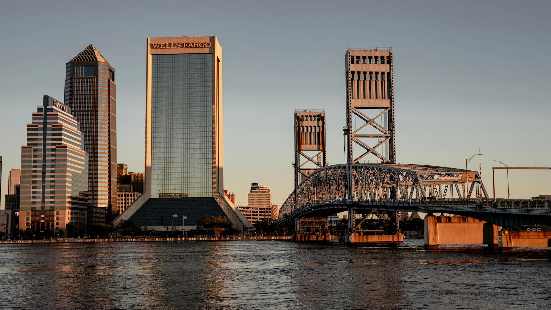 Stunning view of Jacksonville, FL skyline at sunset with iconic bridges and modern skyscrapers reflecting on the water.