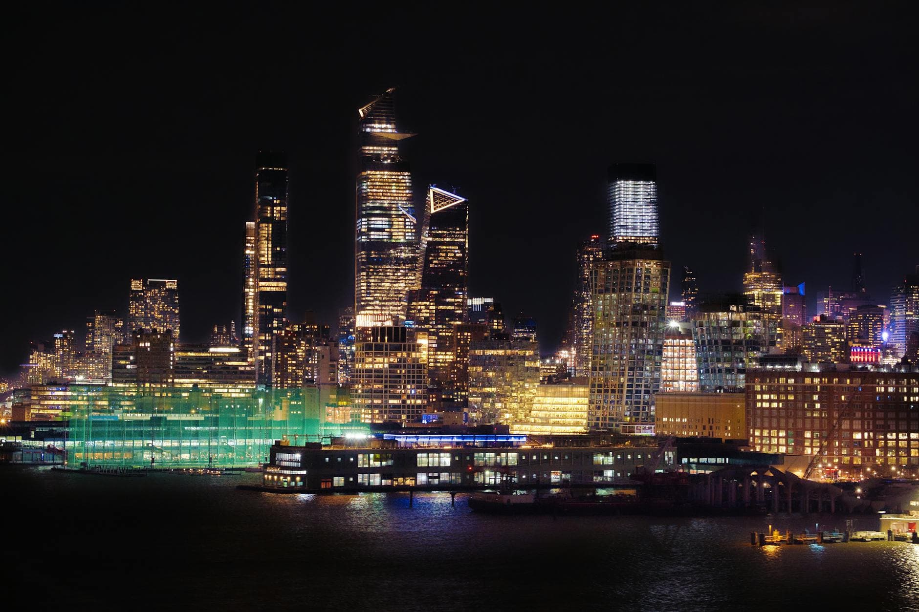 Captivating night cityscape of New York City with illuminated skyscrapers reflecting on the water.