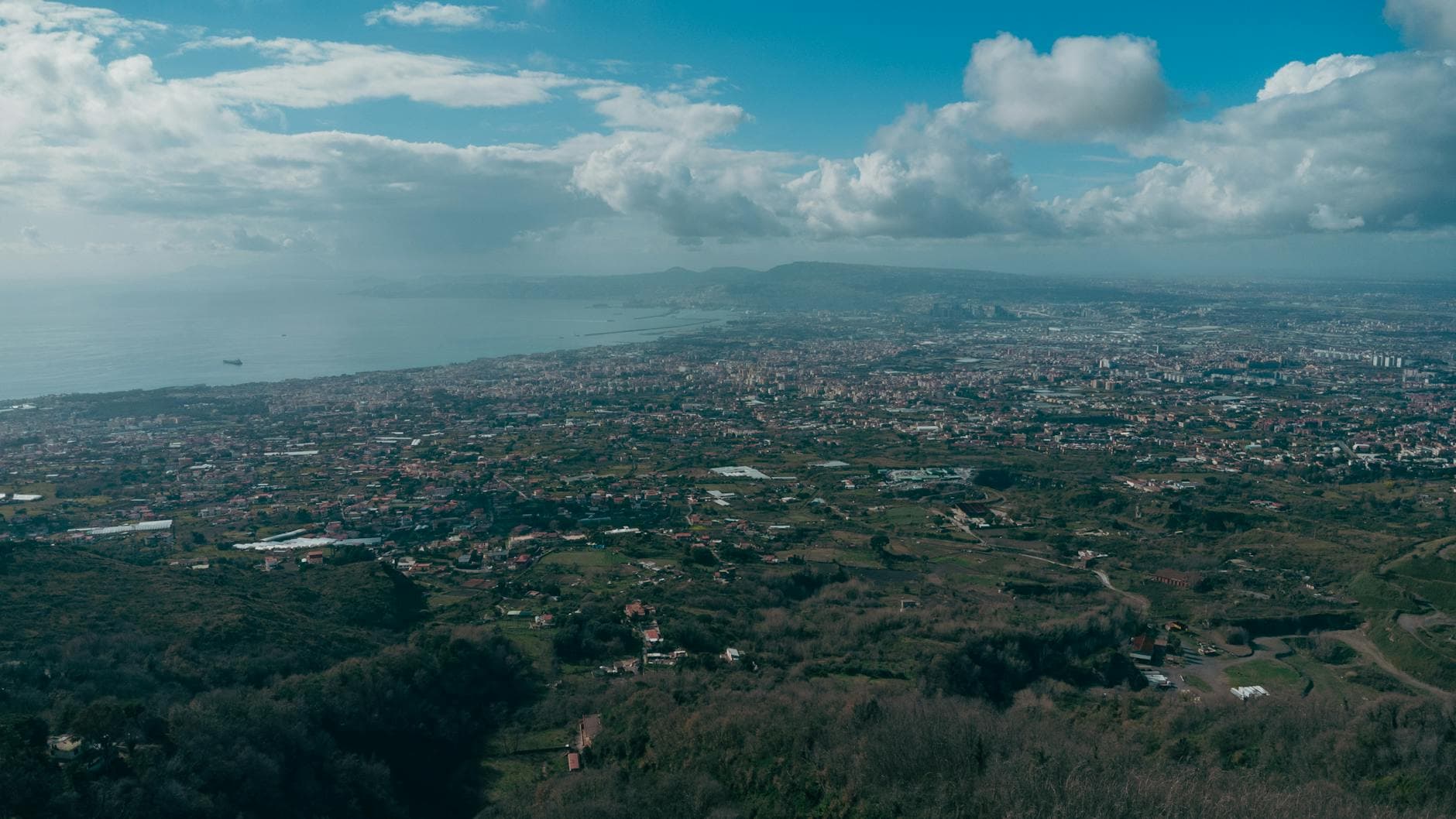 Stunning aerial shot of Naples, Italy, with Mount Vesuvius and the Bay of Naples under a cloudy sky.