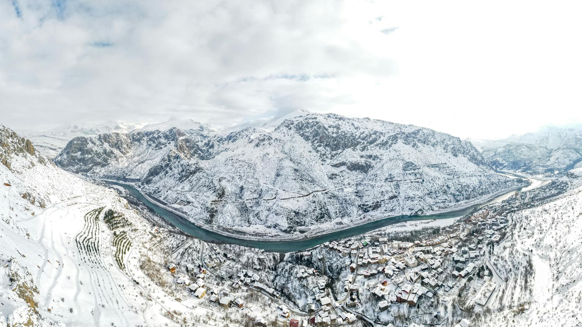 Breathtaking aerial view of a snowy village nestled among majestic mountains and a winding river.