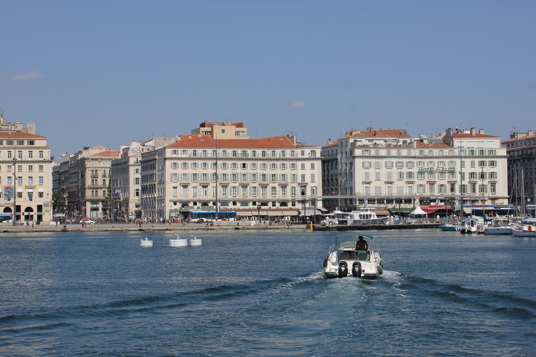 View of Marseille harbor featuring a speedboat and historic buildings on a sunny day, capturing the essence of Mediterranean coastal living.