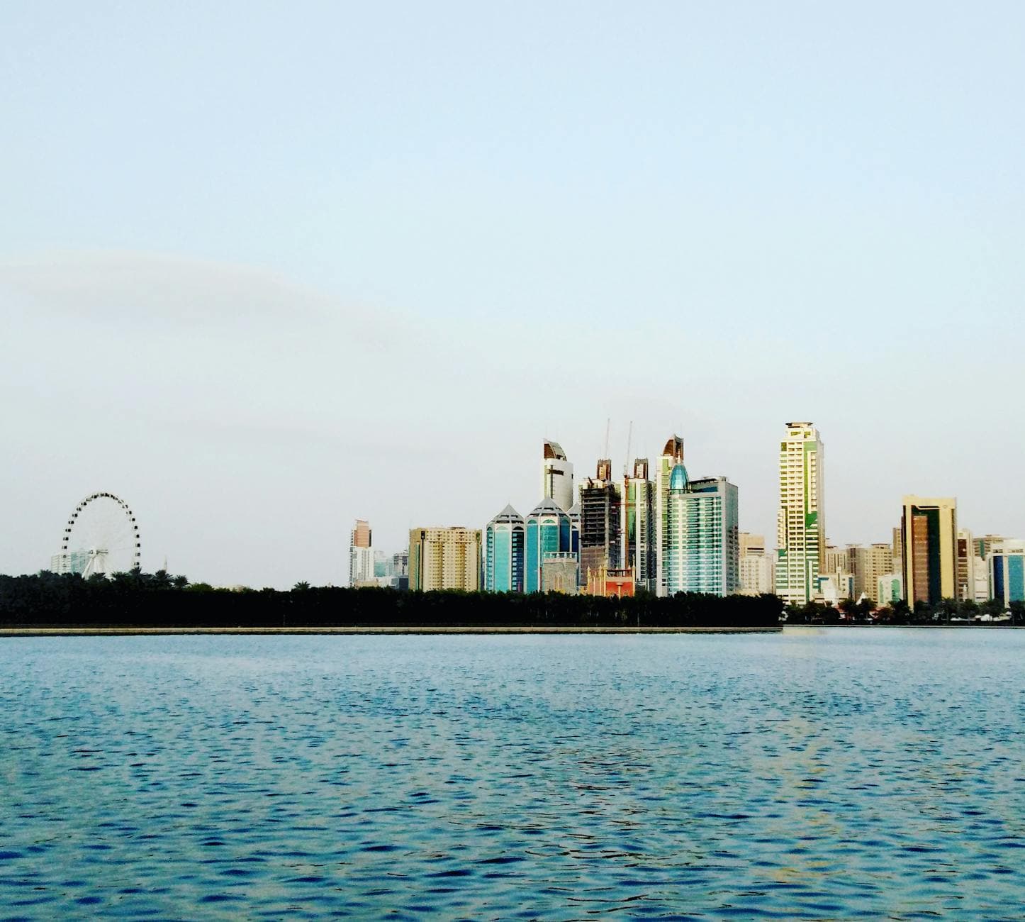 Distant view of Sharjah's modern skyline with a calm waterfront, showcasing urban architecture in the UAE.