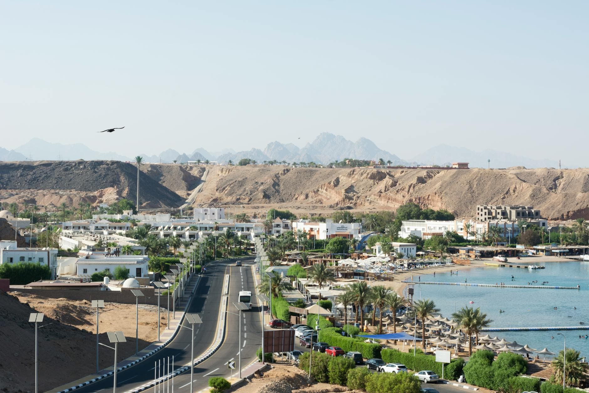 A panoramic aerial view of the Sharm El Sheikh coastline and surrounding cityscape, featuring sandy desert hills.