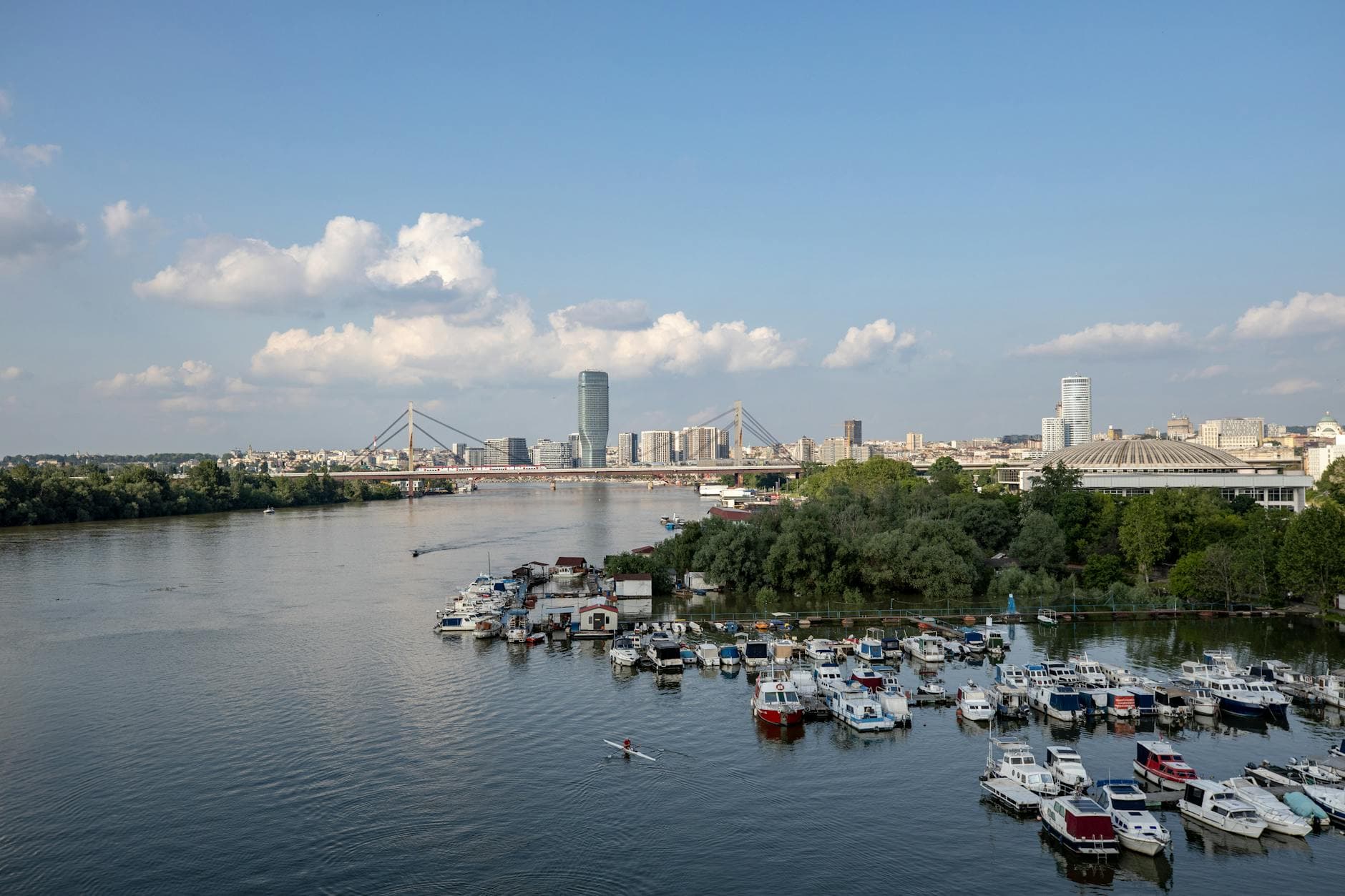 A serene scene of Belgrade's skyline and marina on the Sava River under a clear blue sky.